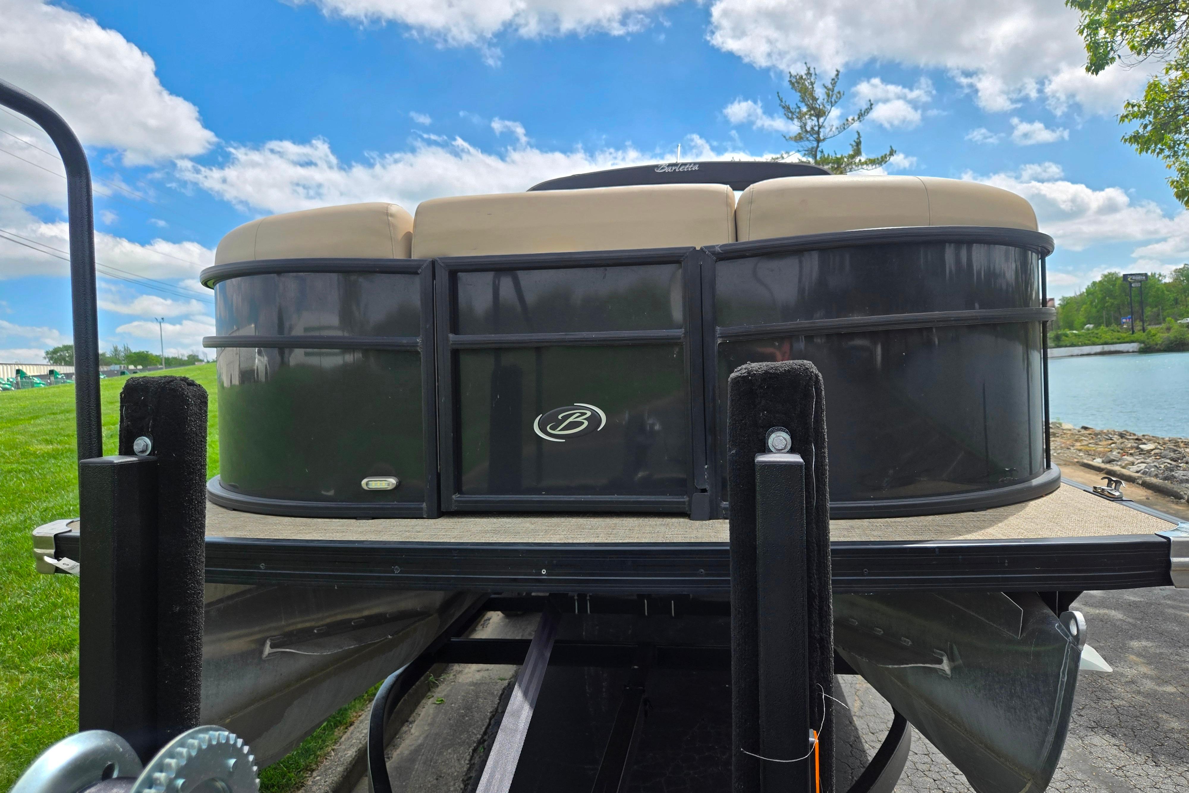 2021 Barletta C22QC pontoon boat on trailer, parked near a lake under a blue sky.