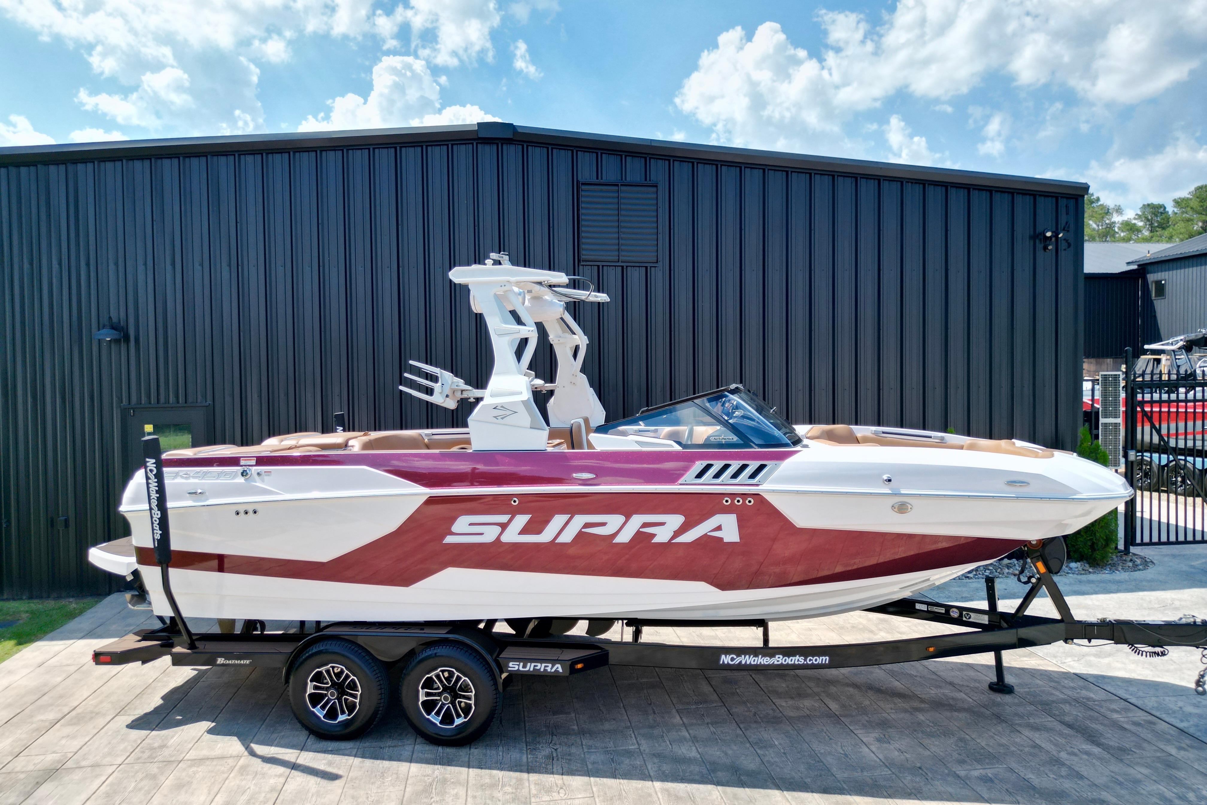 2021 Supra SE boat on trailer, parked outside a black building under a blue sky.