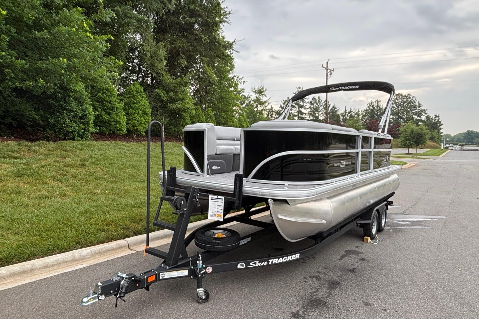 2026 Sun Tracker Party Barge 20 DLX pontoon boat on trailer, parked near greenery.