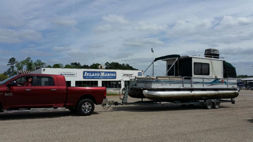 A red pickup truck towing a Sun Tracker party boat on a trailer in front of a marine store.