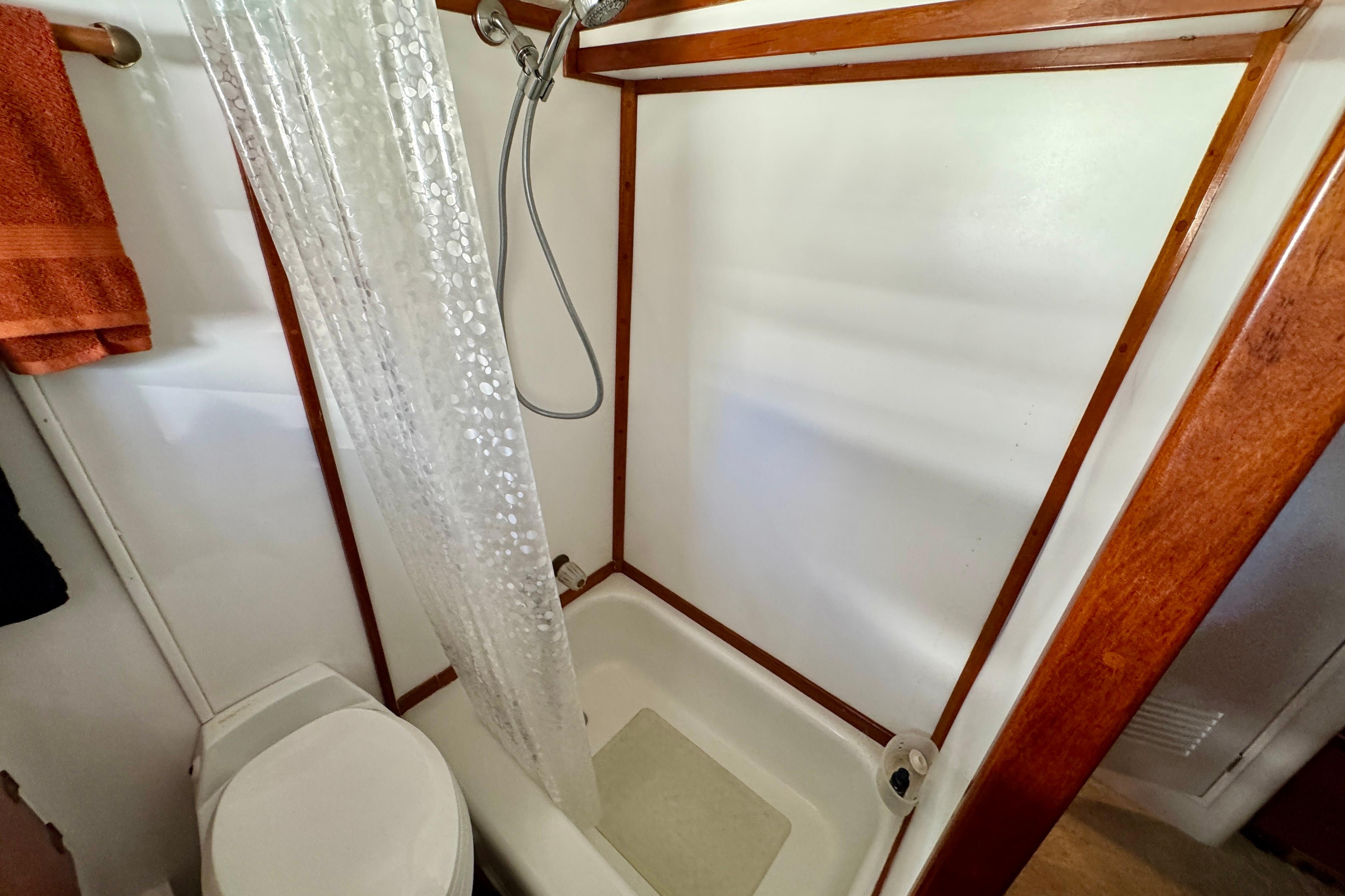 1958 Blanchard Pilothouse bathroom with shower, wooden trim, and orange towel.