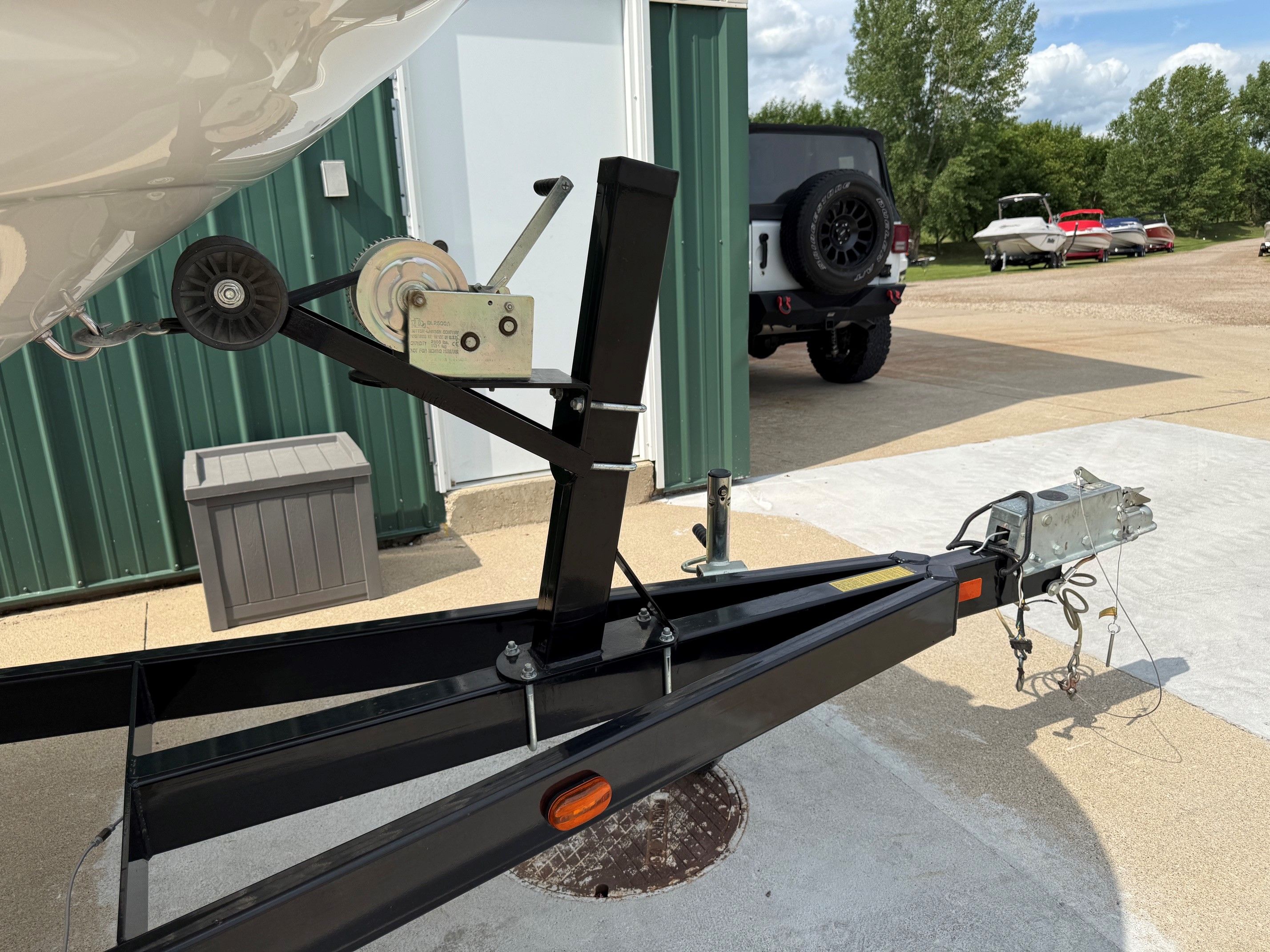 A boat trailer with a winch, parked on a concrete lot next to a green building.