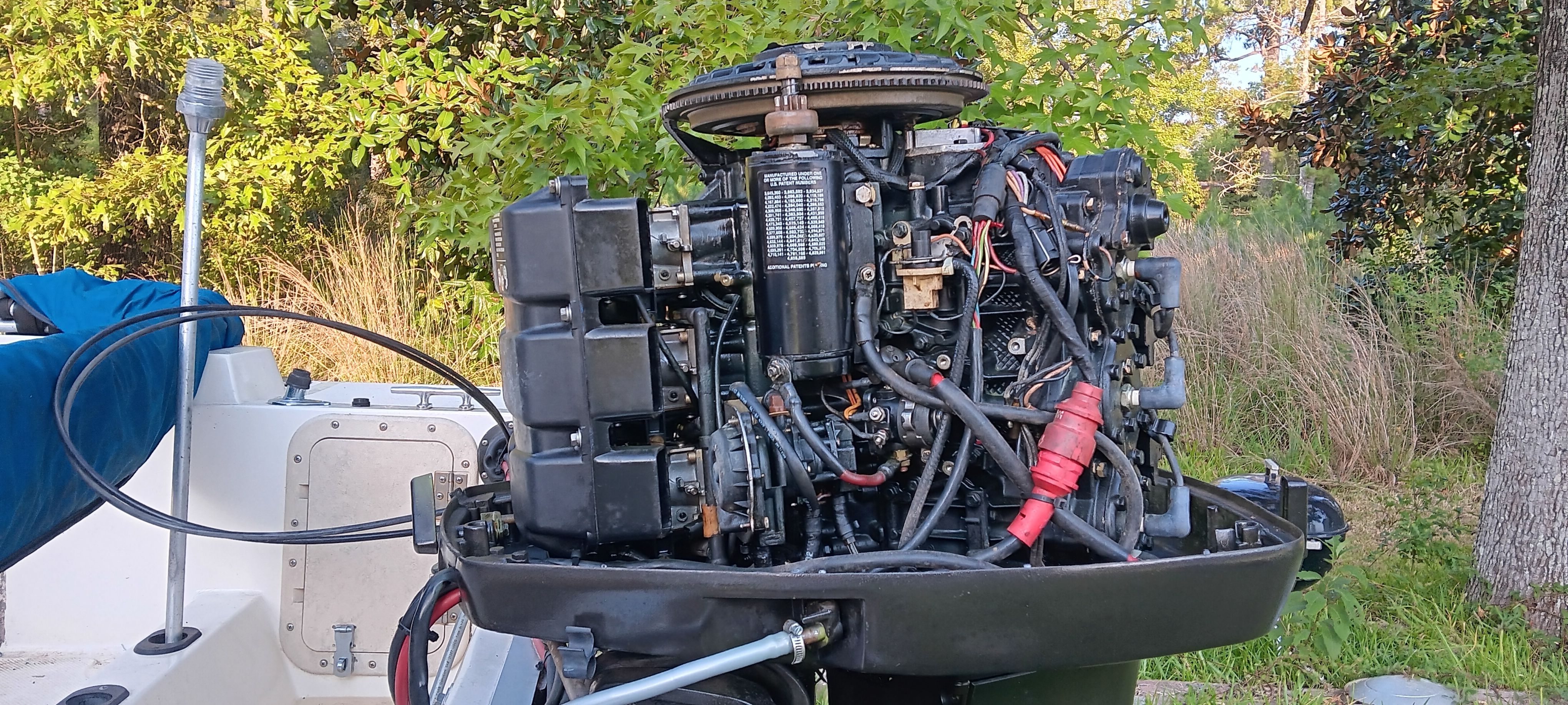 An exposed boat engine with visible components, surrounded by trees and grass.