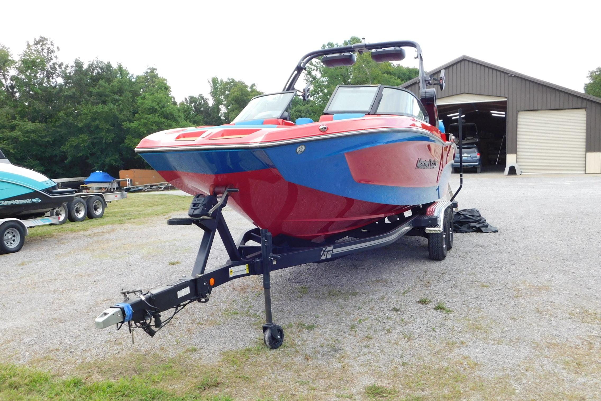 2022 MasterCraft NXT24 boat on trailer, vibrant red and blue design, parked outdoors.