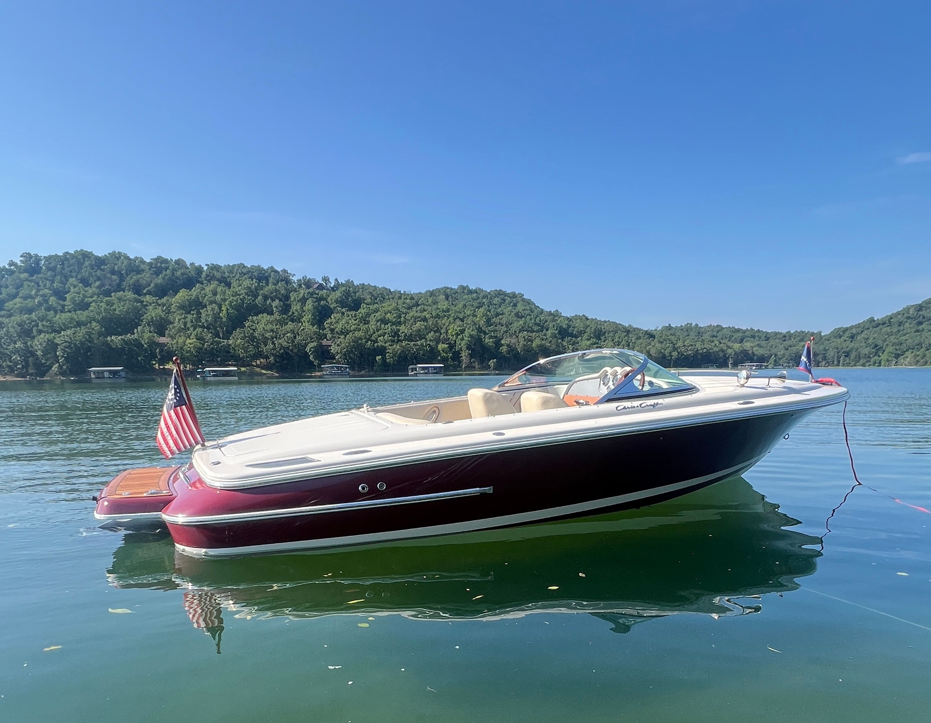 A 2006 Chris-Craft Speedster 20 floats on a calm lake, surrounded by green hills.