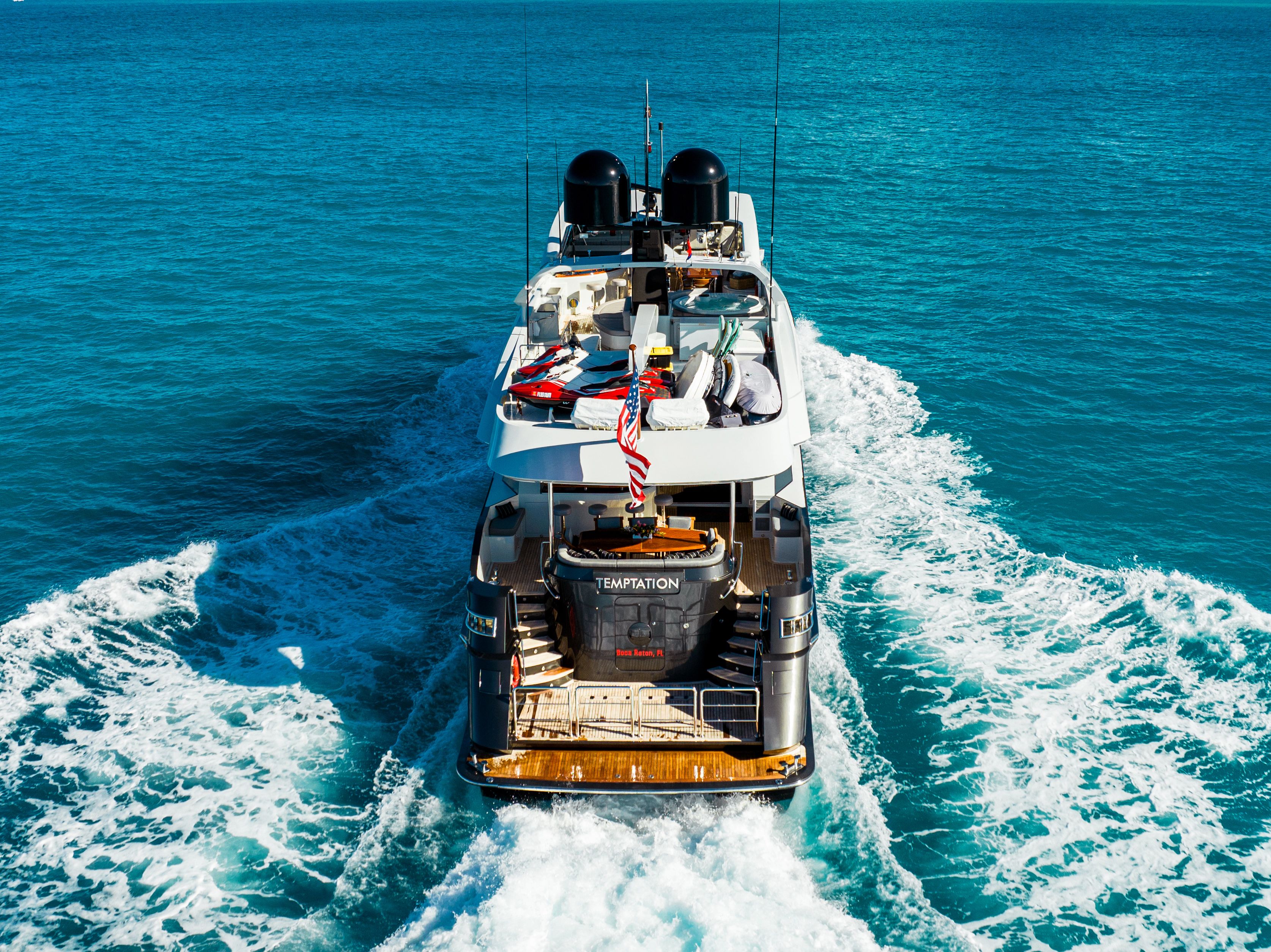 A luxury yacht cruises through turquoise waters, with an American flag at the stern.