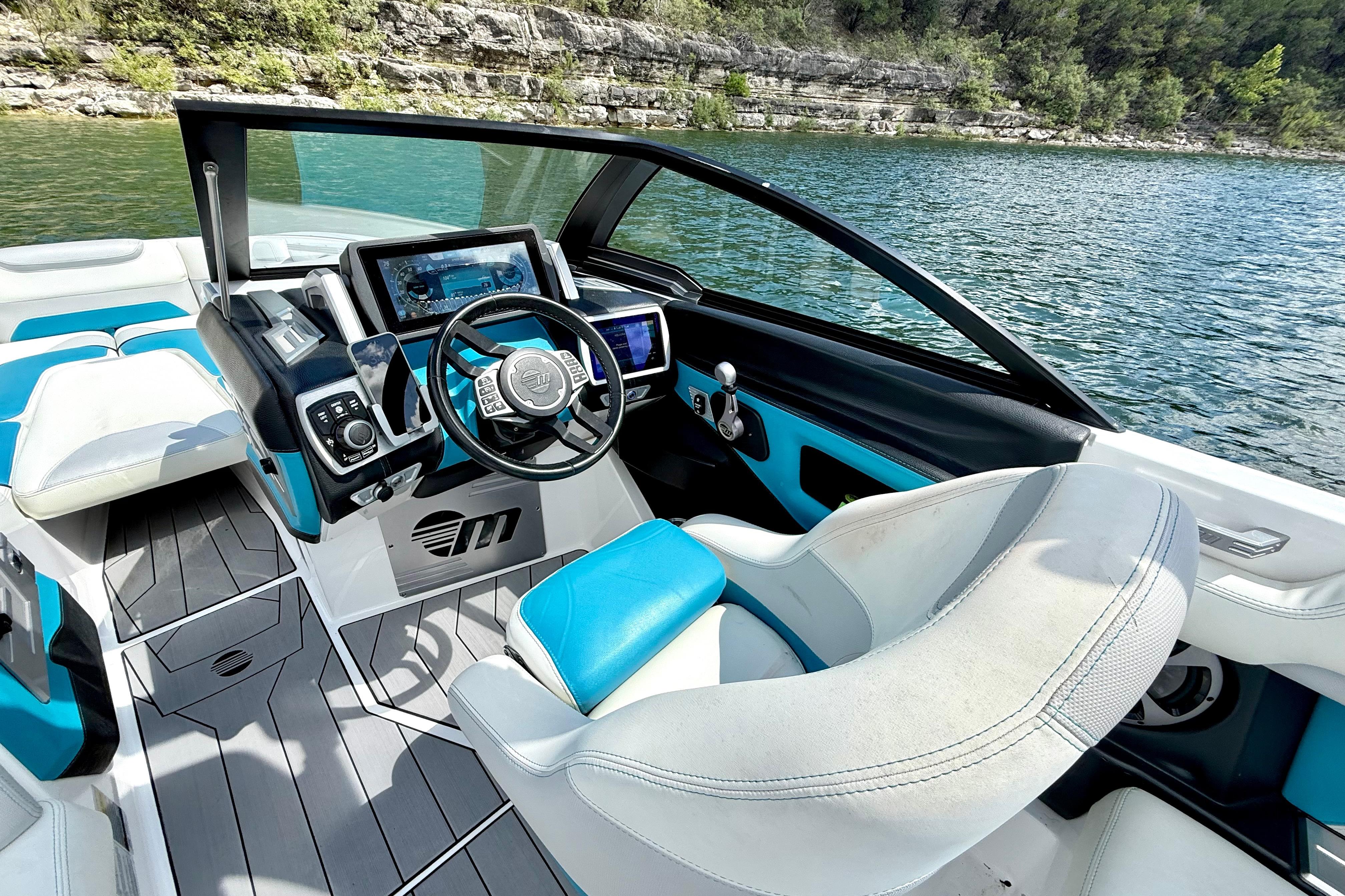 2017 Malibu M235 boat interior with modern dashboard, steering wheel, and blue-white seating by a lake.