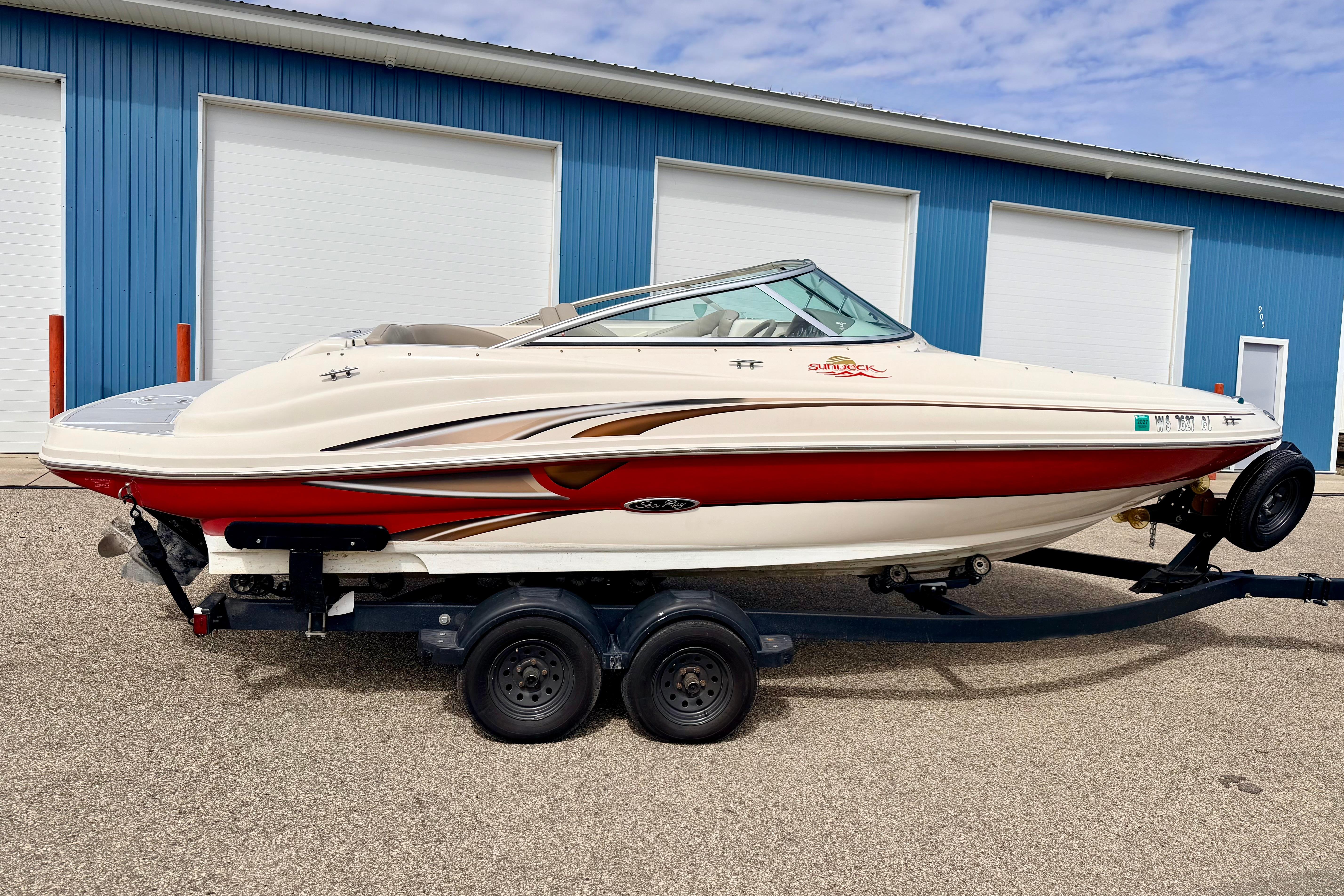 2003 Sea Ray 200 Sundeck boat on trailer, parked outside blue building.