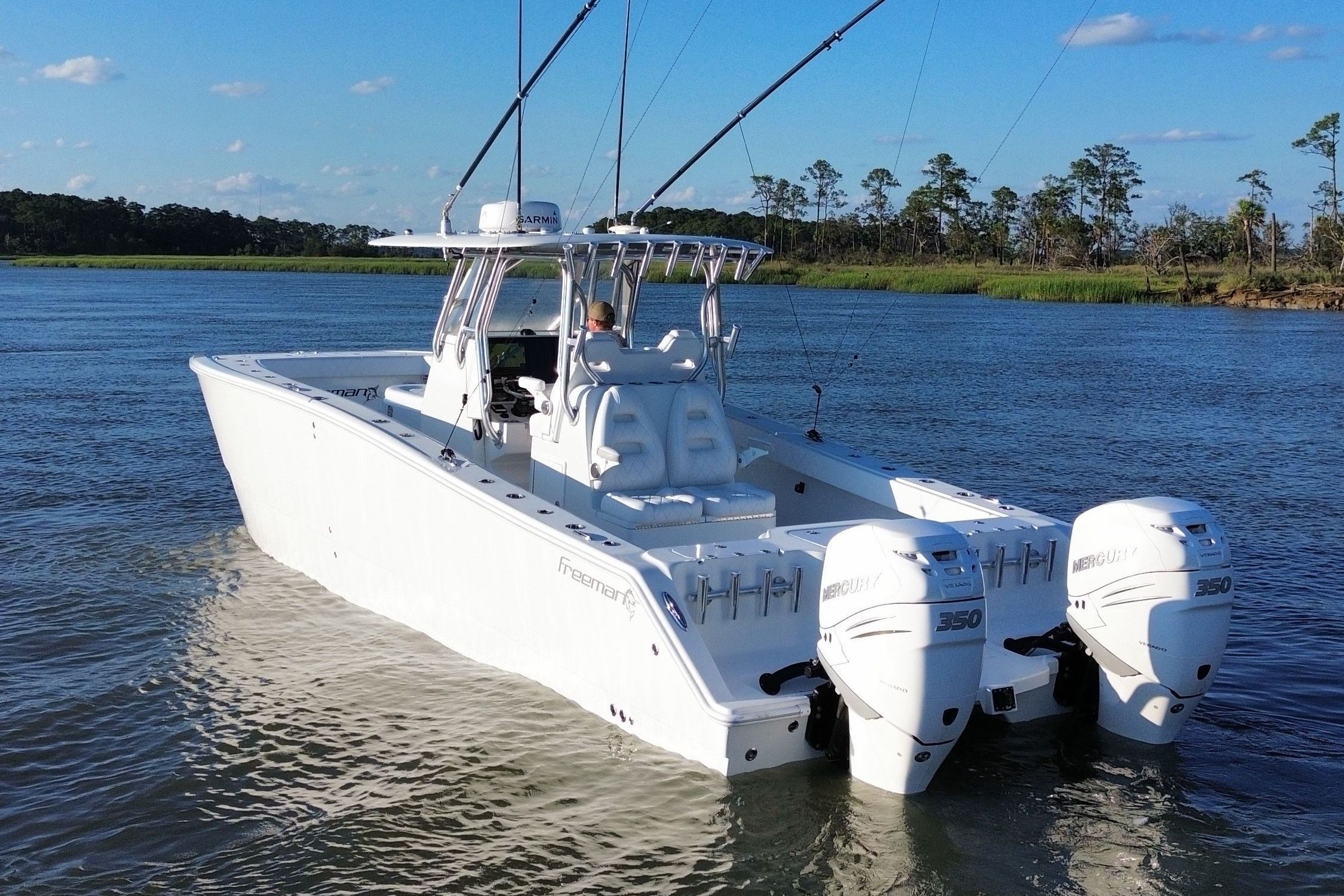 A white boat cruising on calm water, featuring two outboard engines and fishing rods.