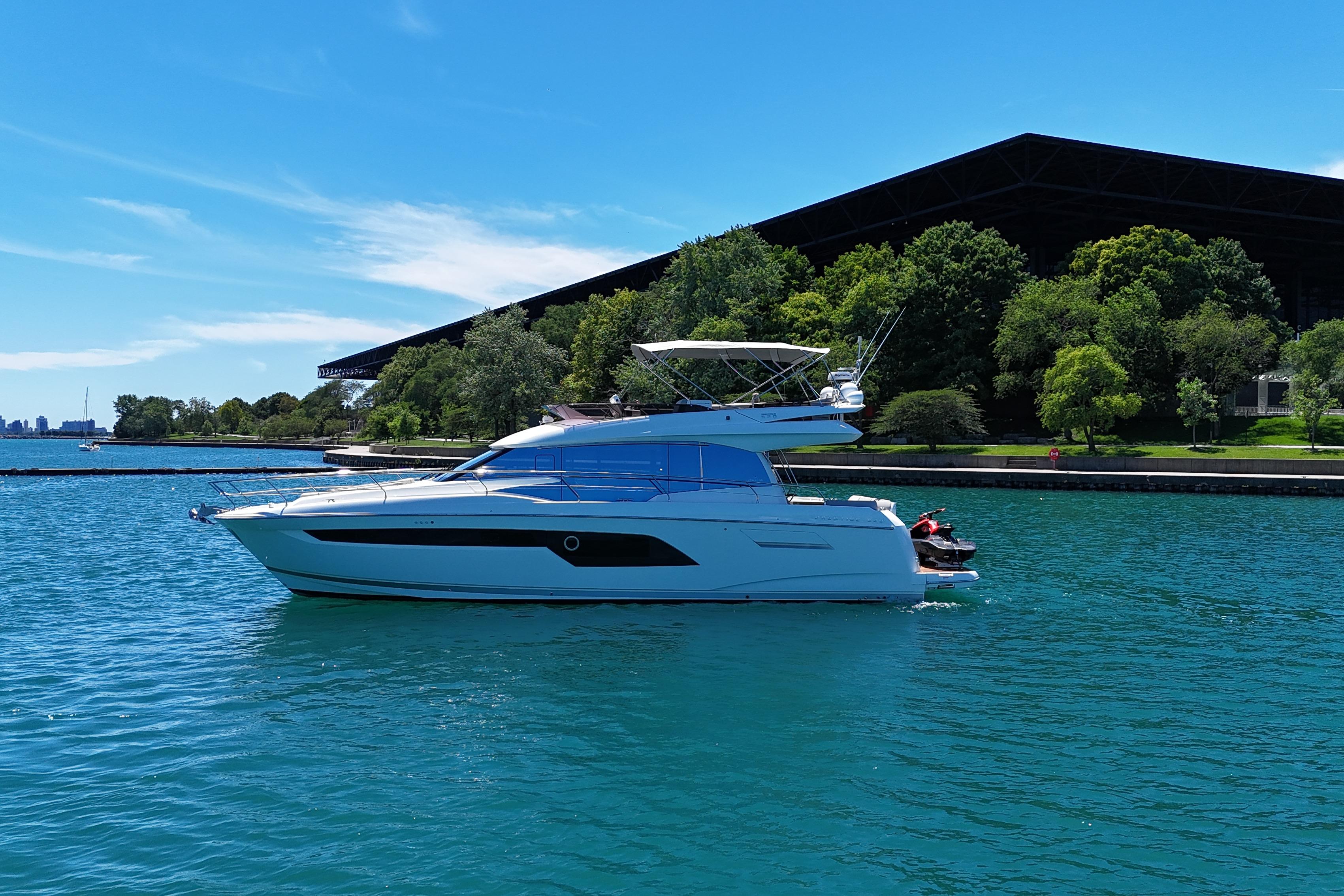 2022 Prestige 520 yacht cruising on a sunny day near lush greenery.