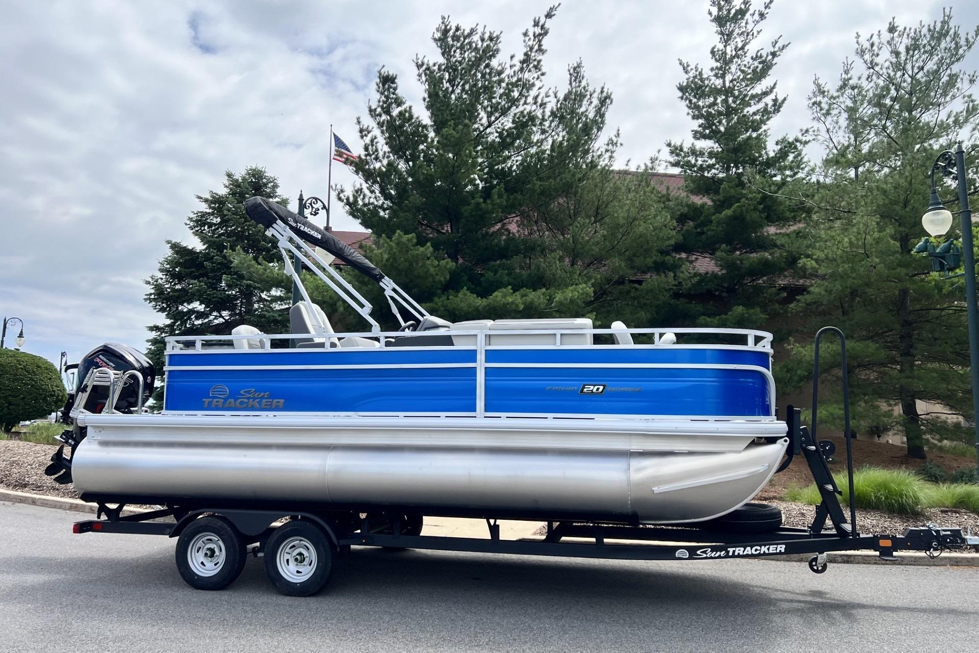 2026 Sun Tracker Fishin' Barge 20 DLX pontoon boat on trailer, parked outdoors.