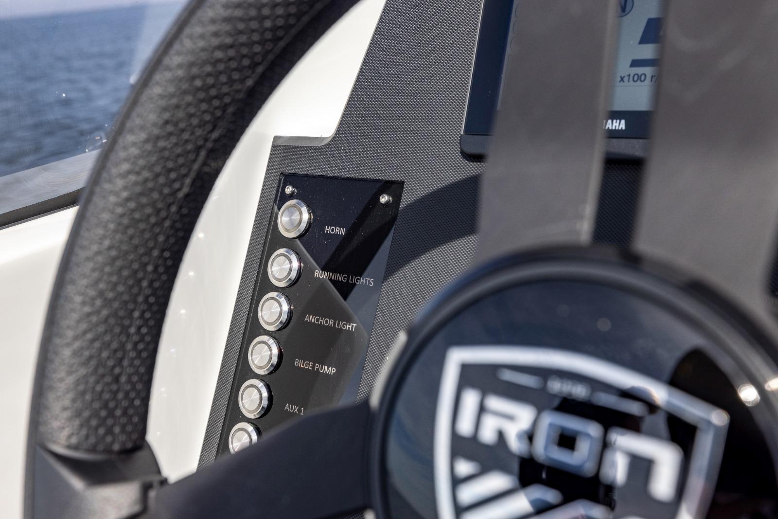 Close-up of Iron 707 boat dashboard with control buttons, steering wheel, and sea in background.