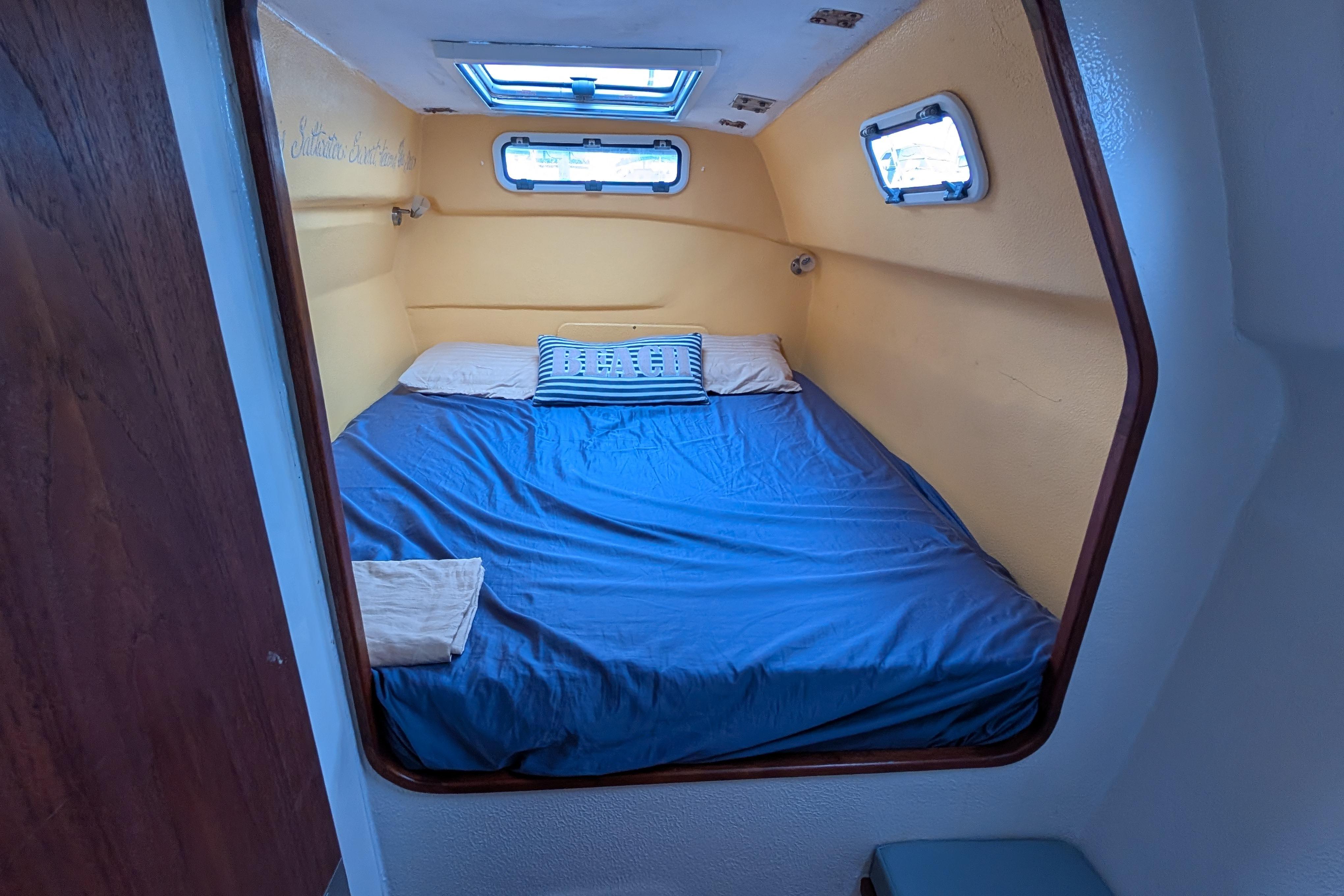 Cozy cabin interior of 1999 Island Spirit 37 sailboat with blue bedding and portholes.