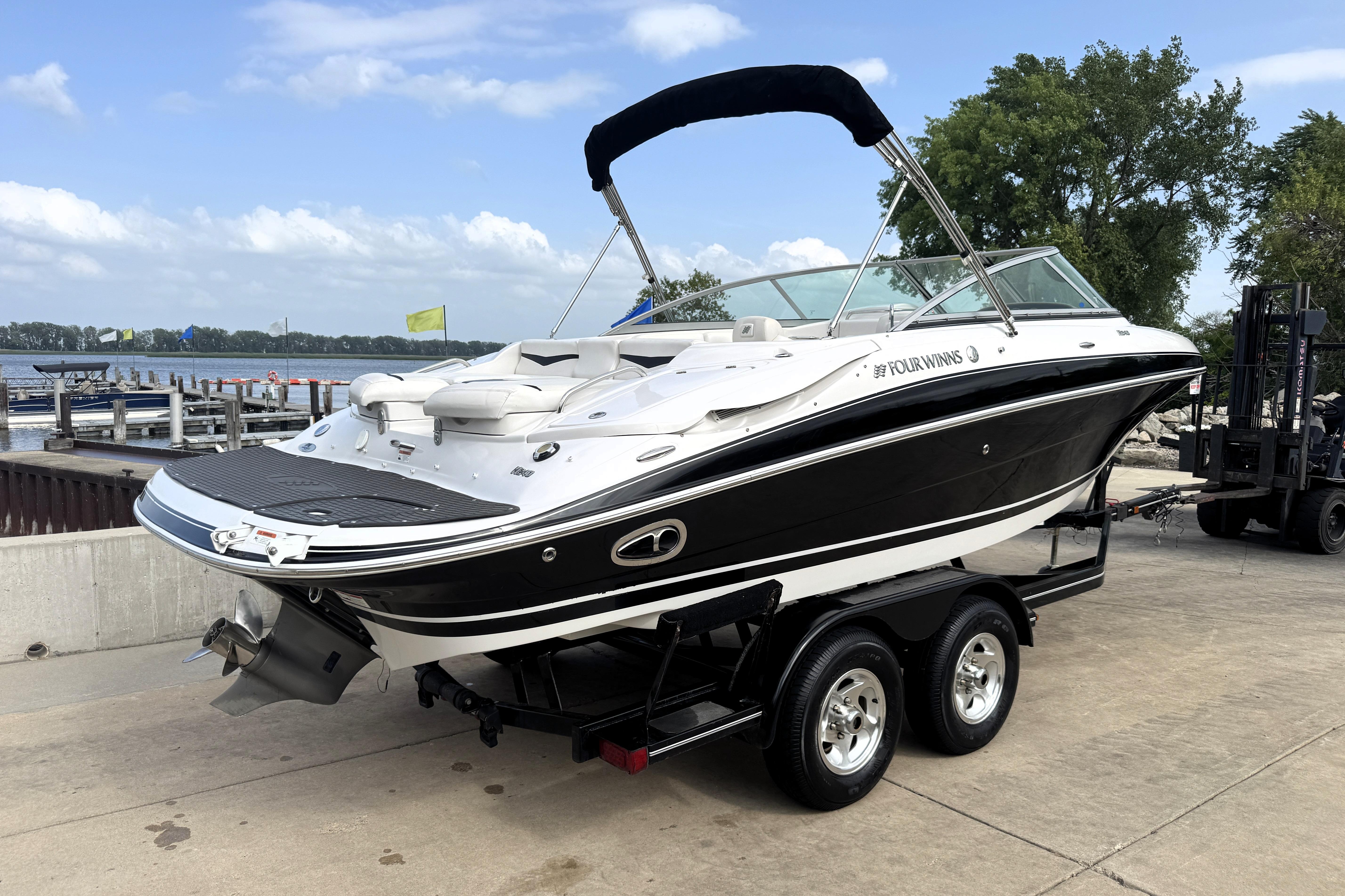 2008 Four Winns H240 boat on trailer by lakeside, featuring sleek black and white design.