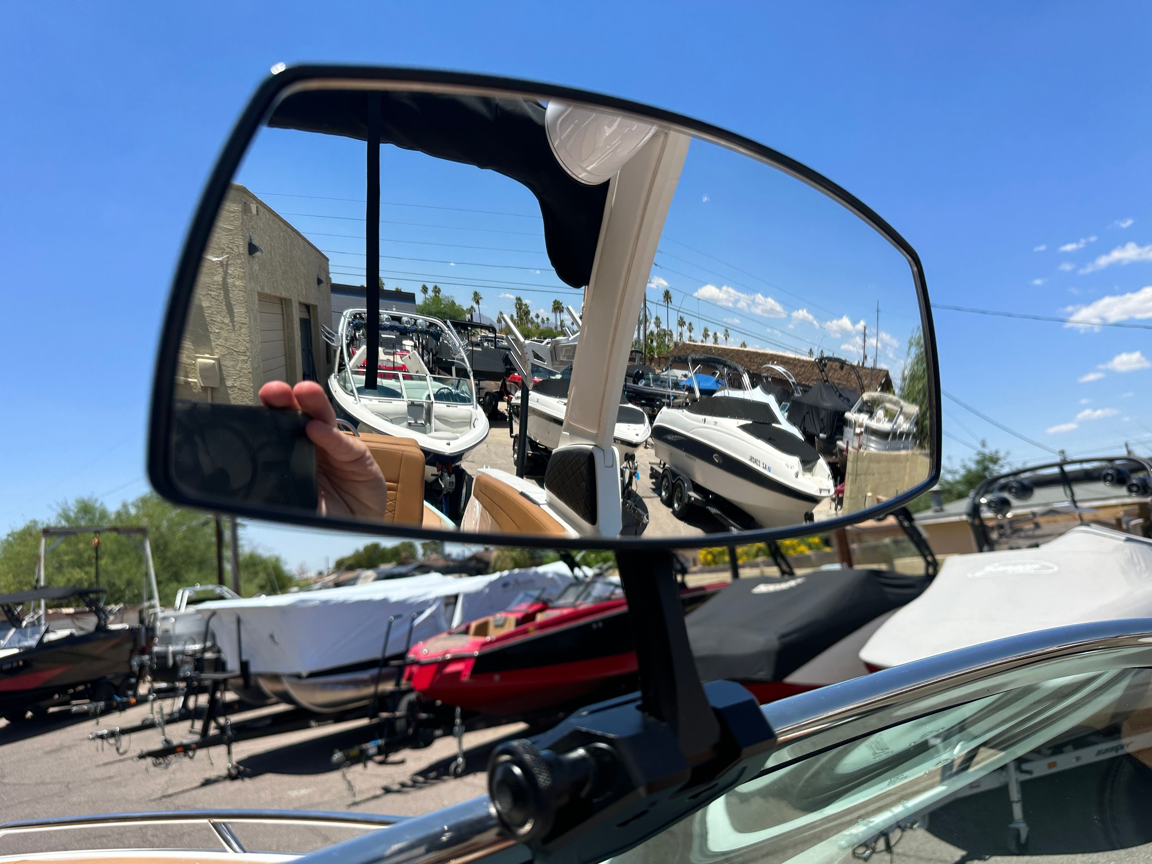 Boat's rearview mirror reflects several boats in a parking lot on a sunny day.