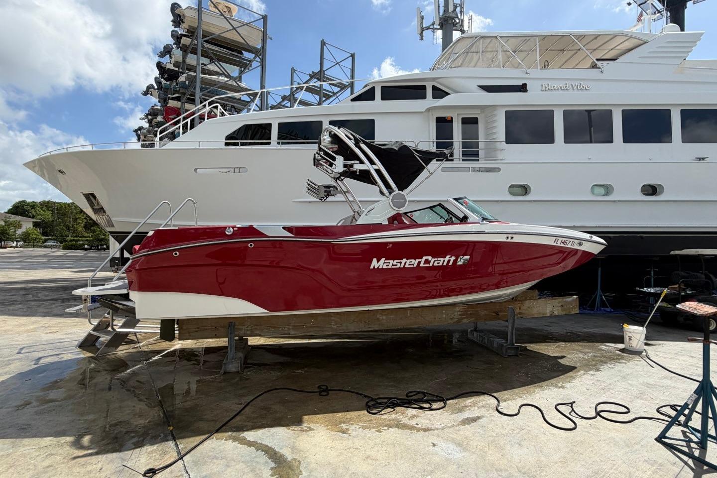 2023 MasterCraft X24 boat in vibrant red, docked beside a large yacht.