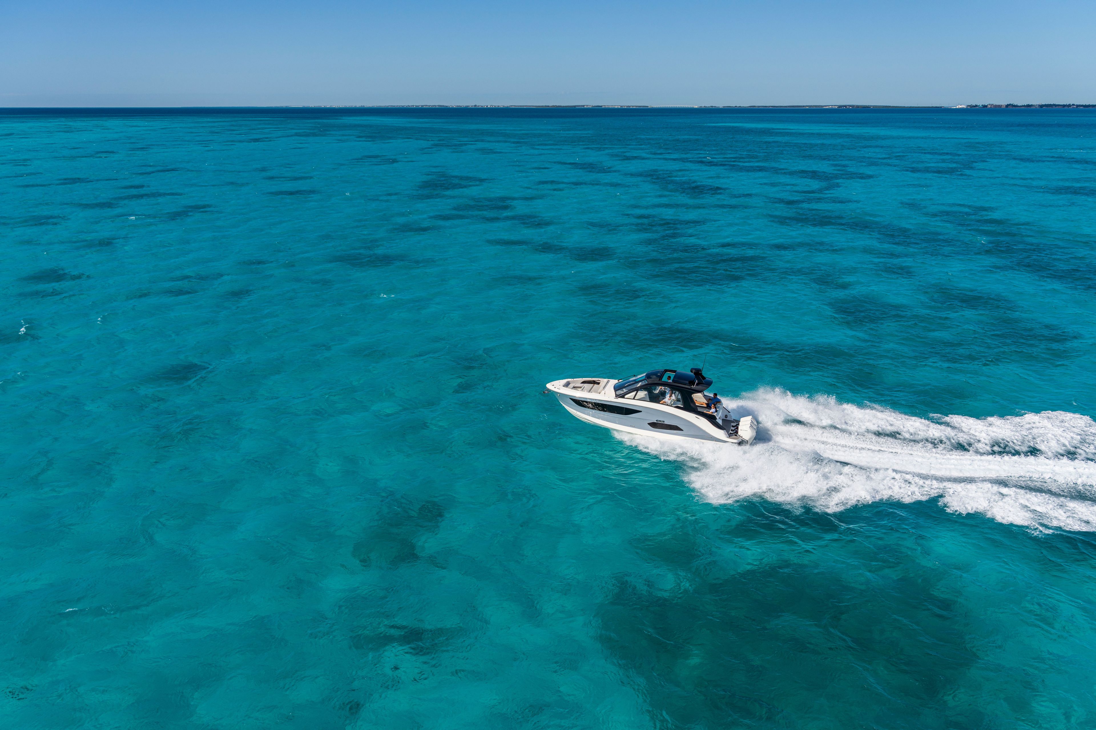 Sea Ray Sundancer 370 Outboard speeding across turquoise water under a clear sky.