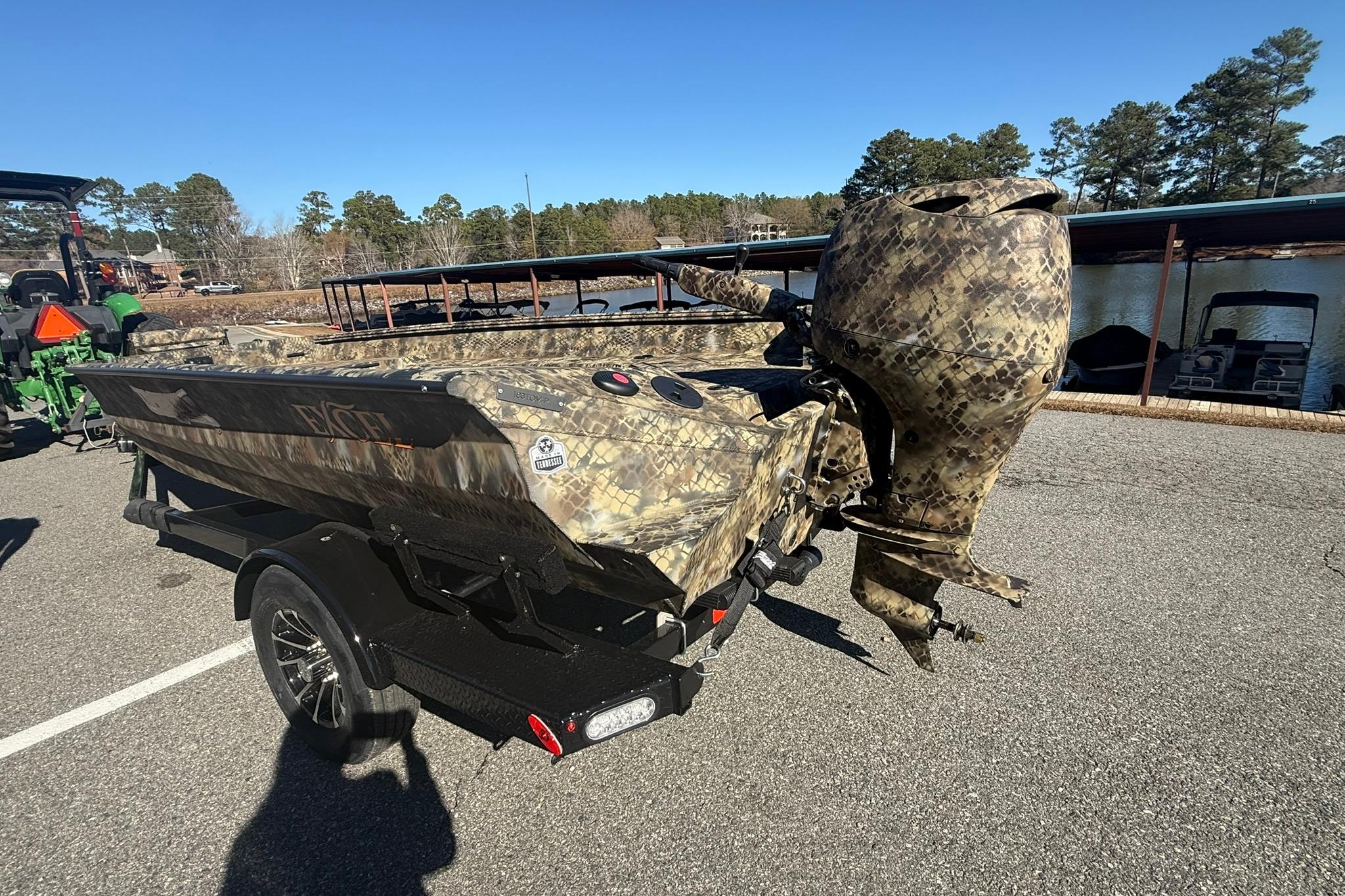 Camouflage-patterned 2026 Excel 183 Tomahawk boat on trailer, parked near a lake.