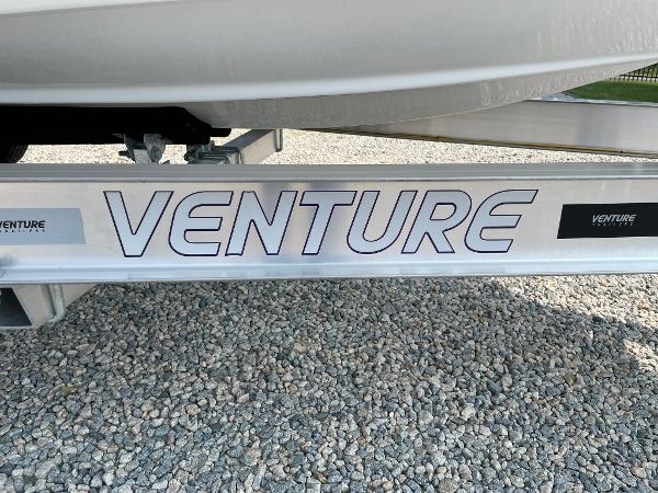 Trailer for 2025 Tidewater 232 CC Adventure boat on gravel surface.