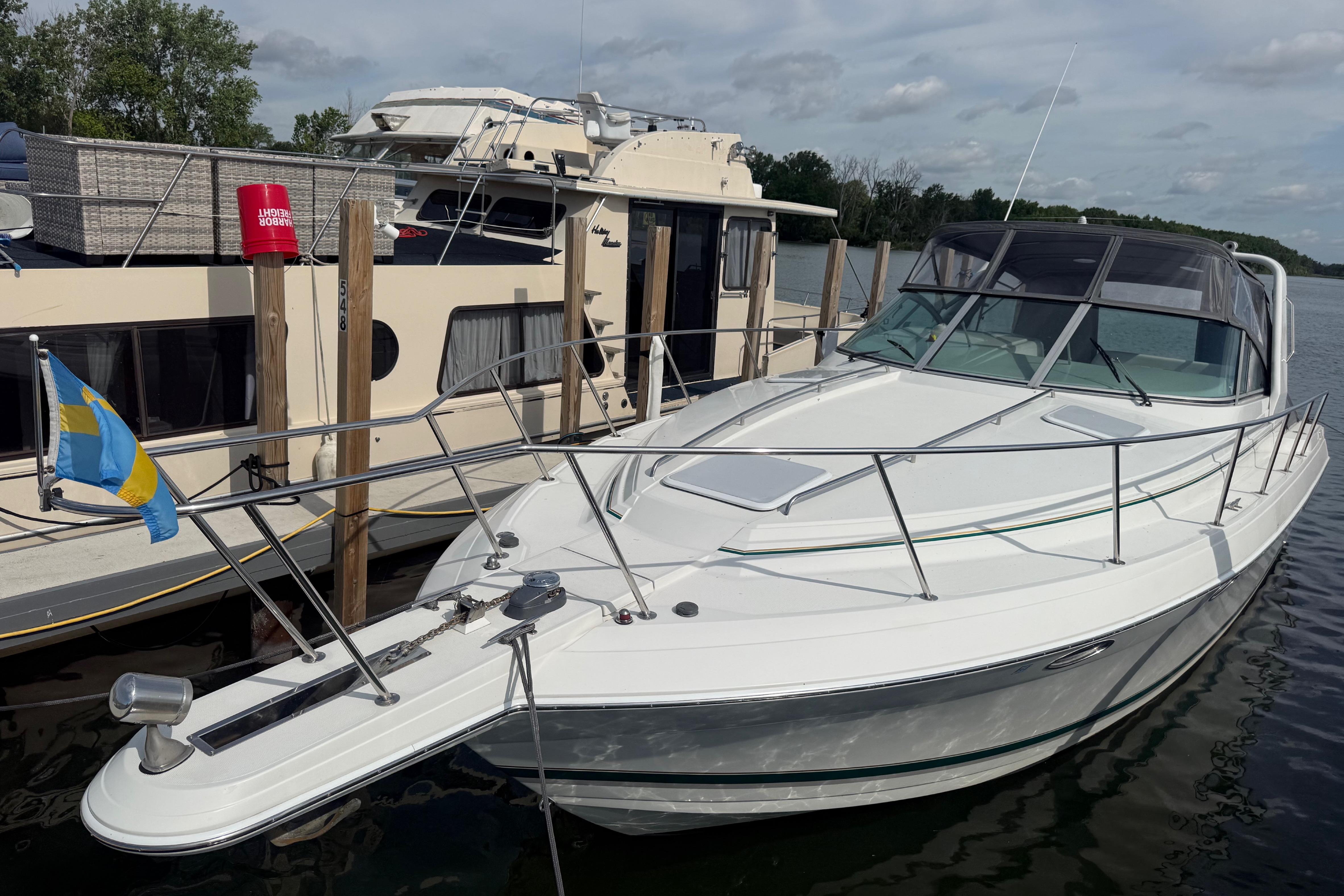1999 Formula 34 Performance Cruiser docked beside a houseboat on a calm river.