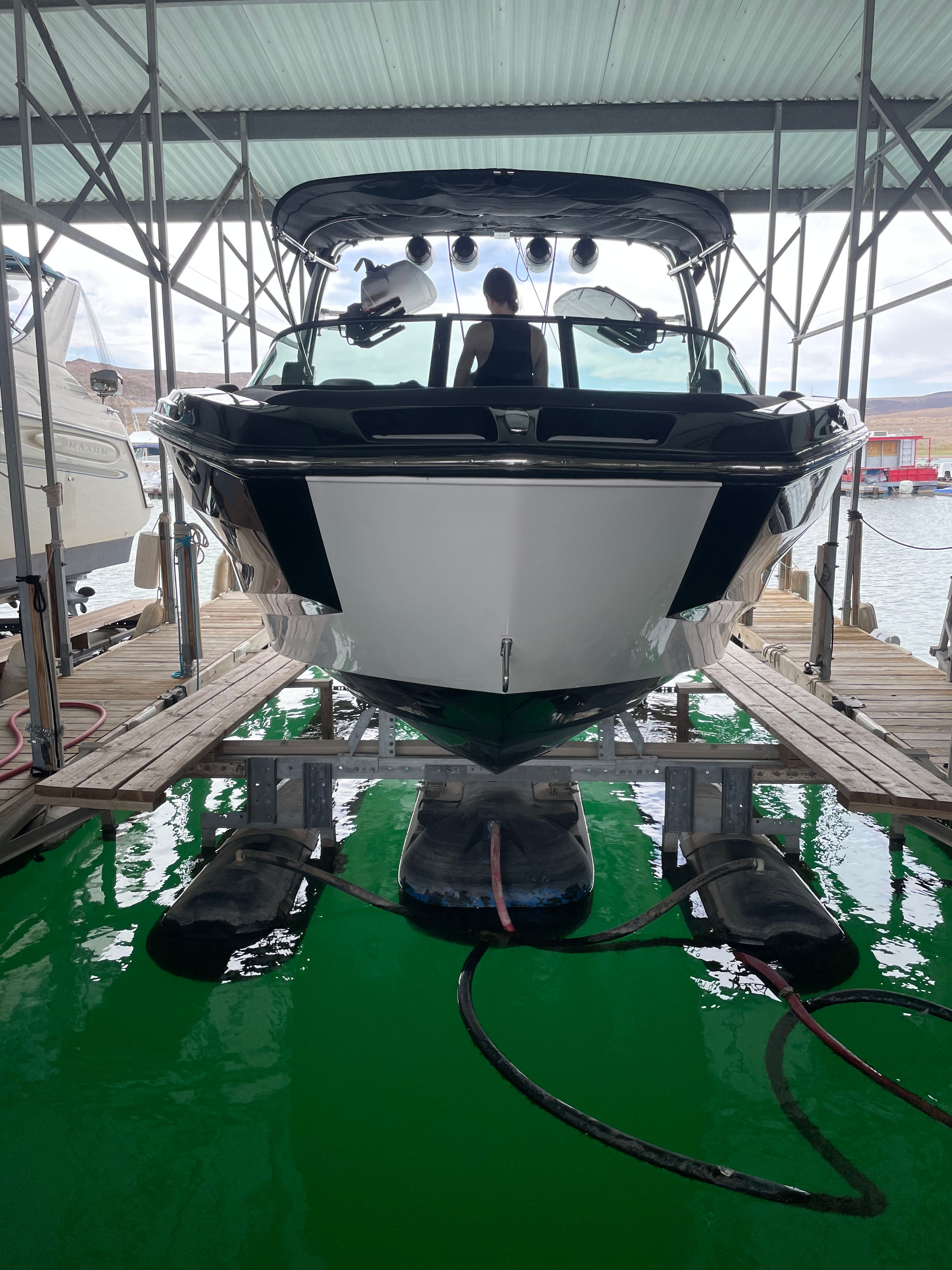 A MasterCraft NXT23 boat is docked under a covered structure on the water.