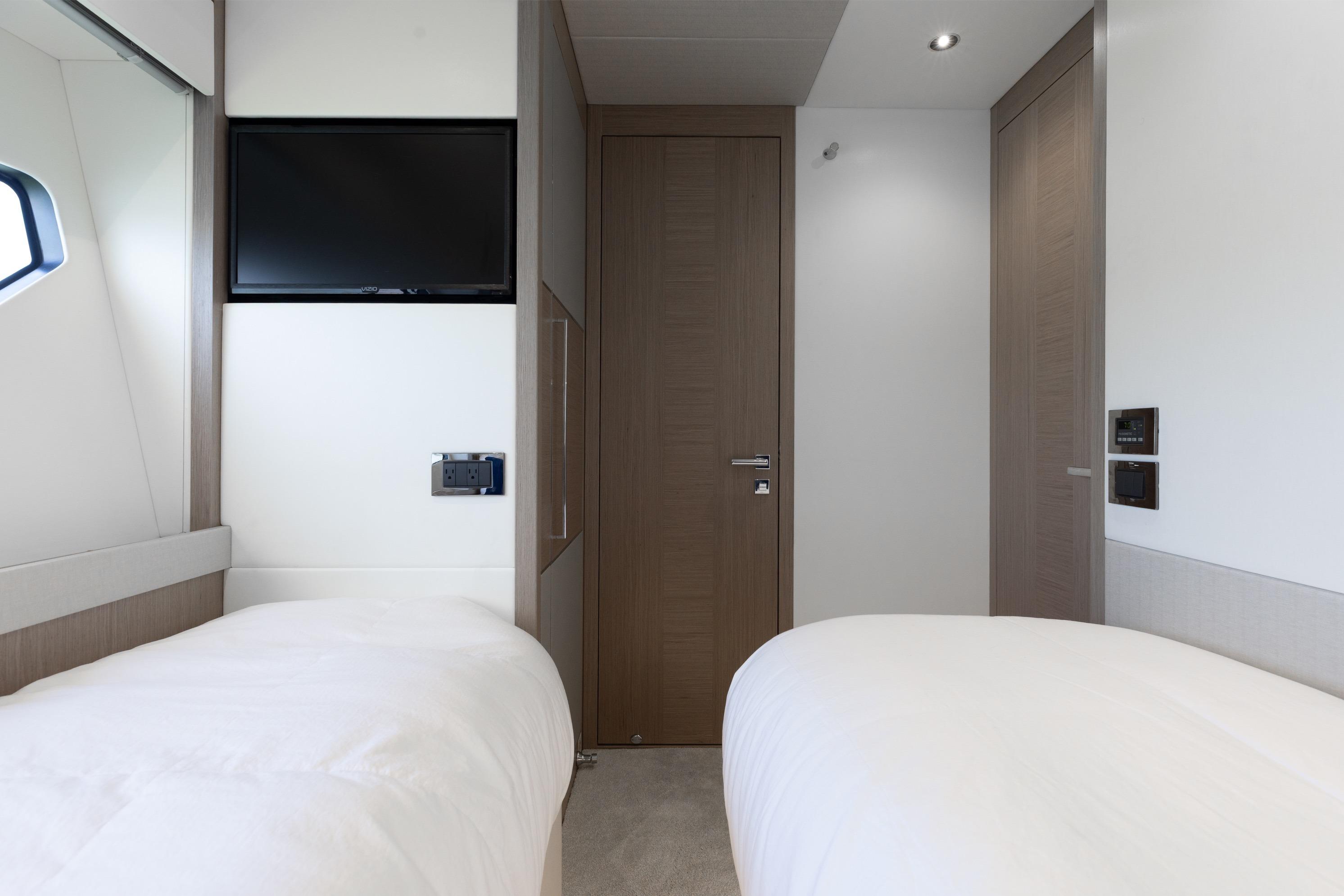 Luxurious twin bedroom in 2022 Sunseeker 76 Yacht with modern decor and TV.
