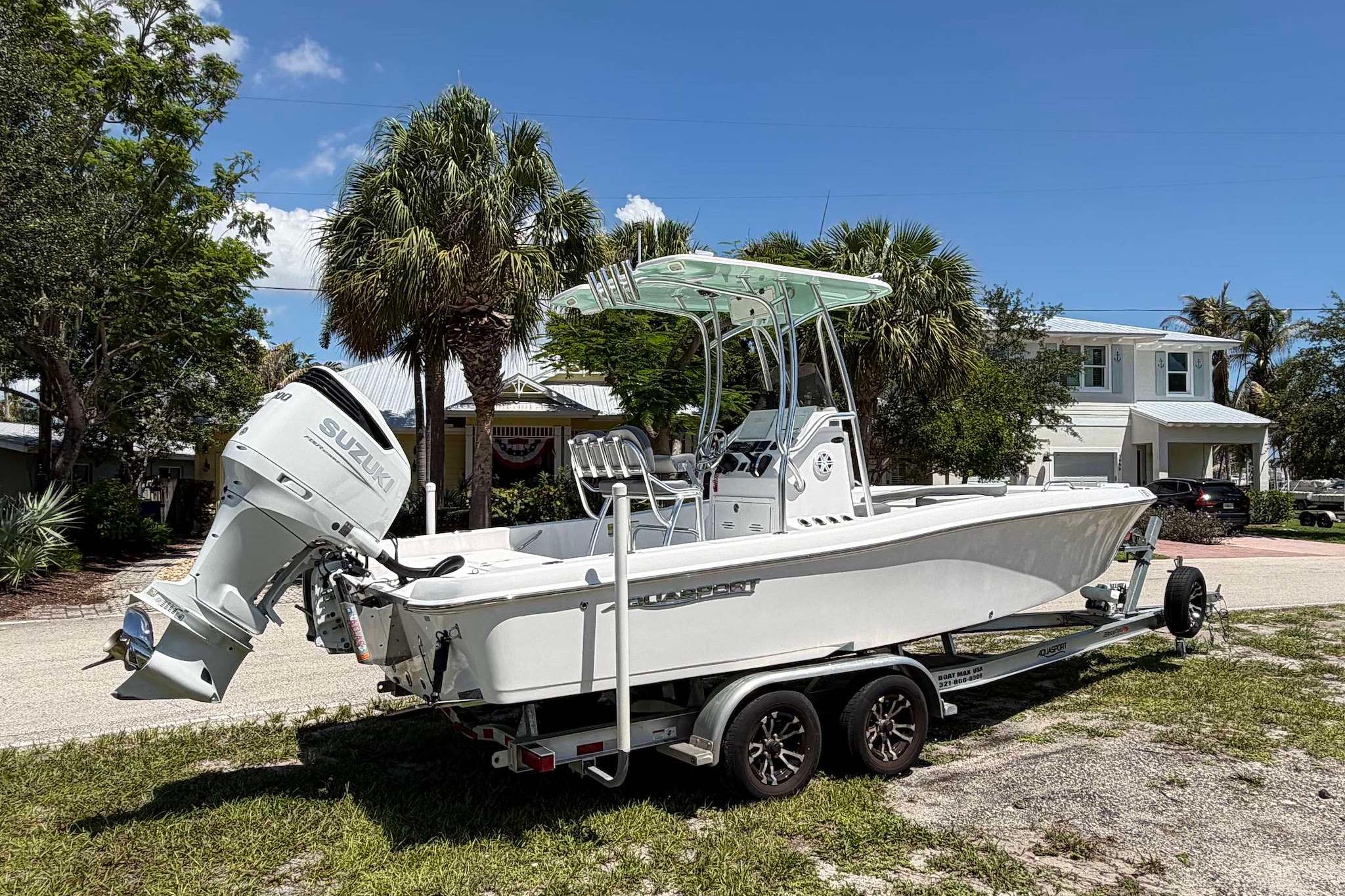 2022 Aquasport 230 Pro Bay boat on trailer, parked near palm trees and houses.