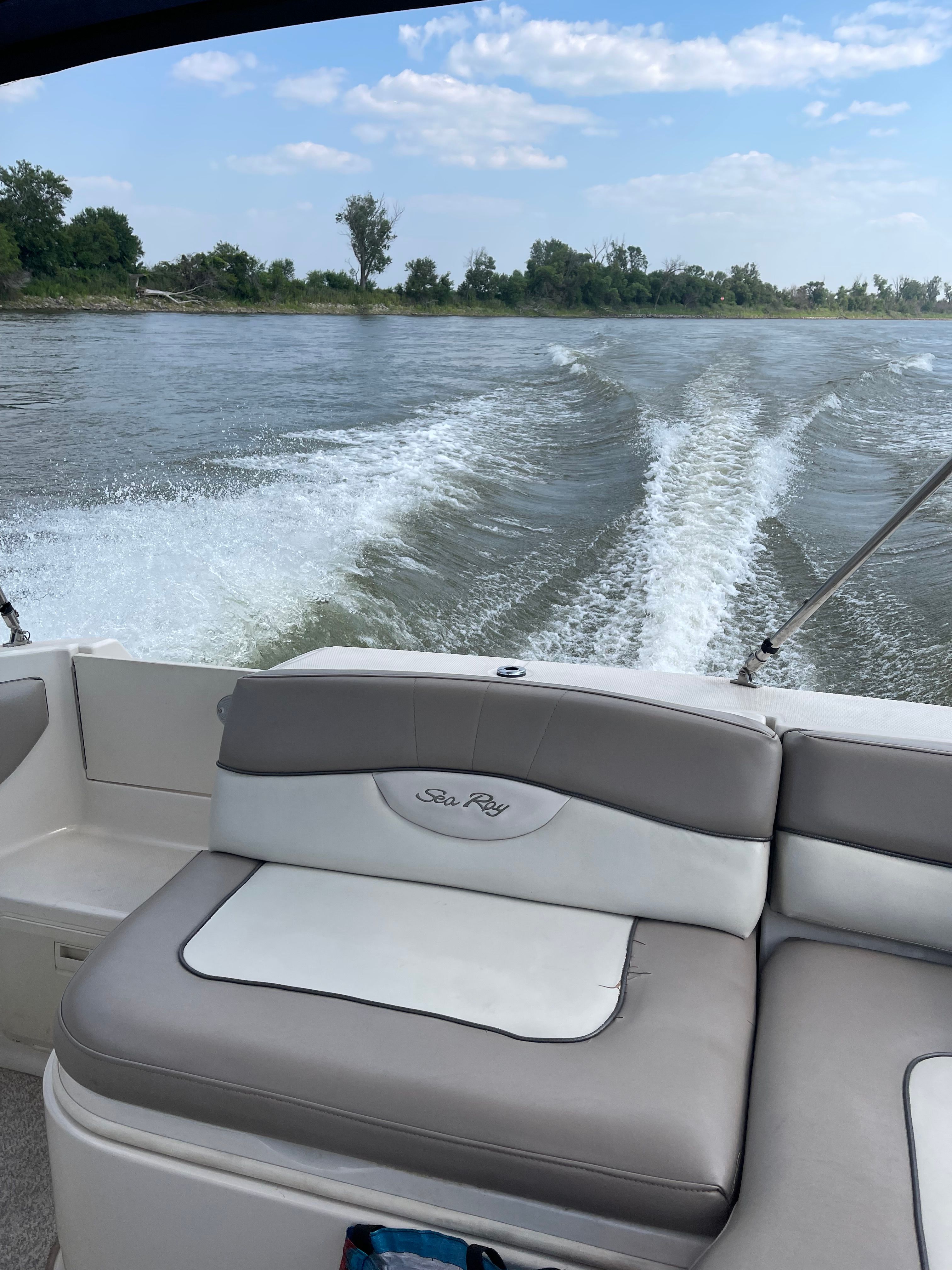 A Sea Ray 220 Sundeck boat on calm water with trees in the background.