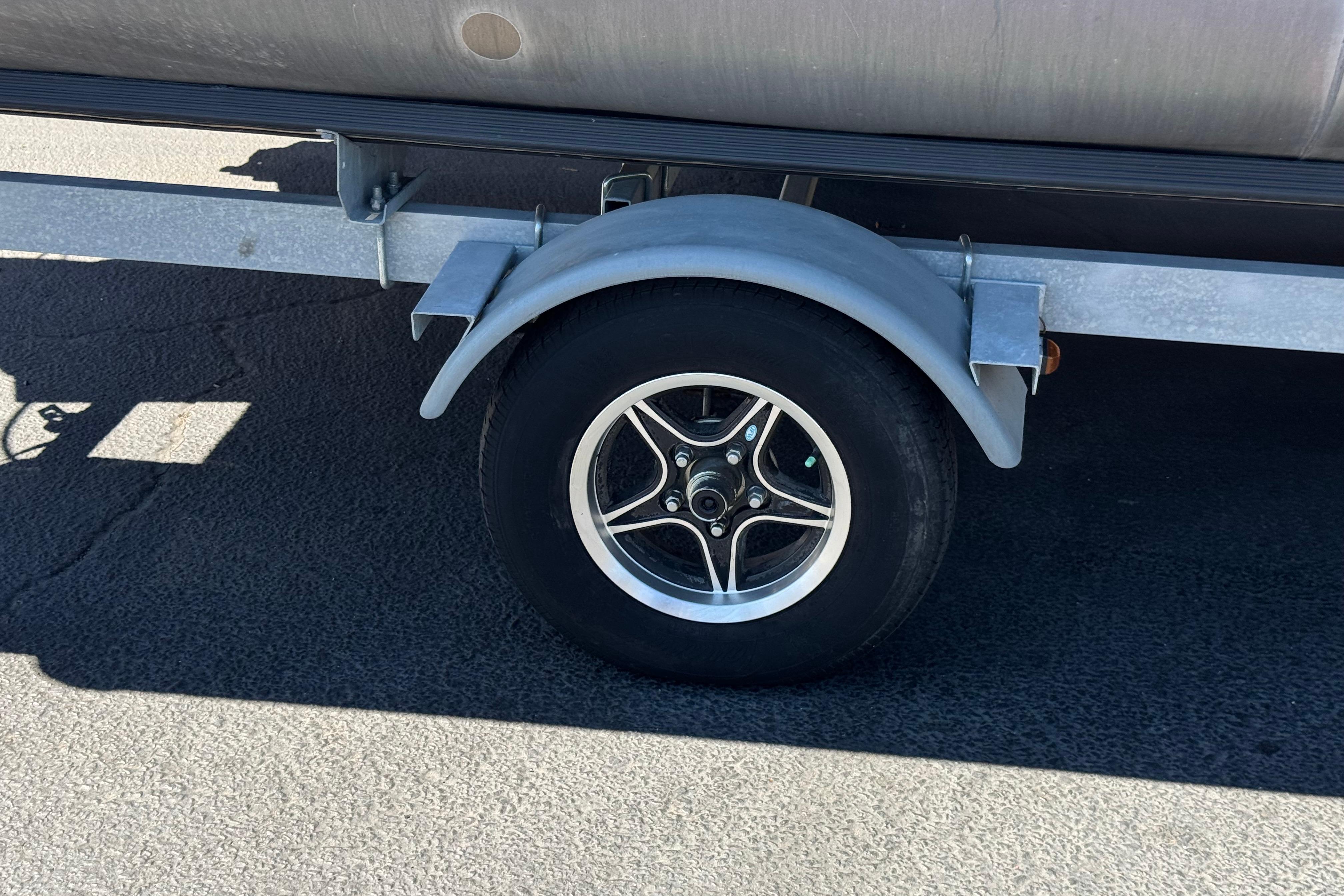 Trailer wheel of 2023 Avalon Venture Fish N Cruise boat on asphalt.