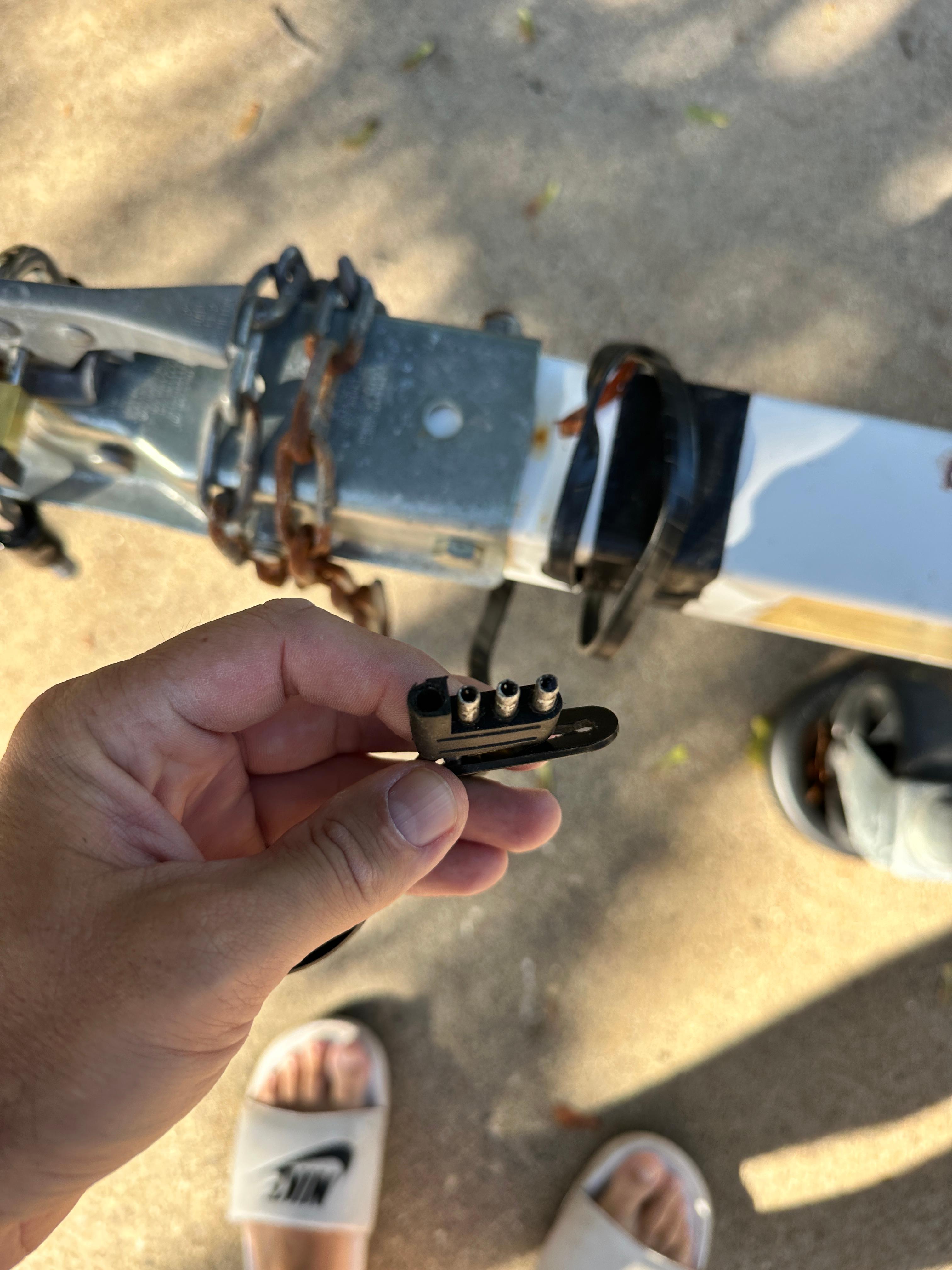 Hand holding a trailer connector near a Lund H model trailer hitch, 1960.