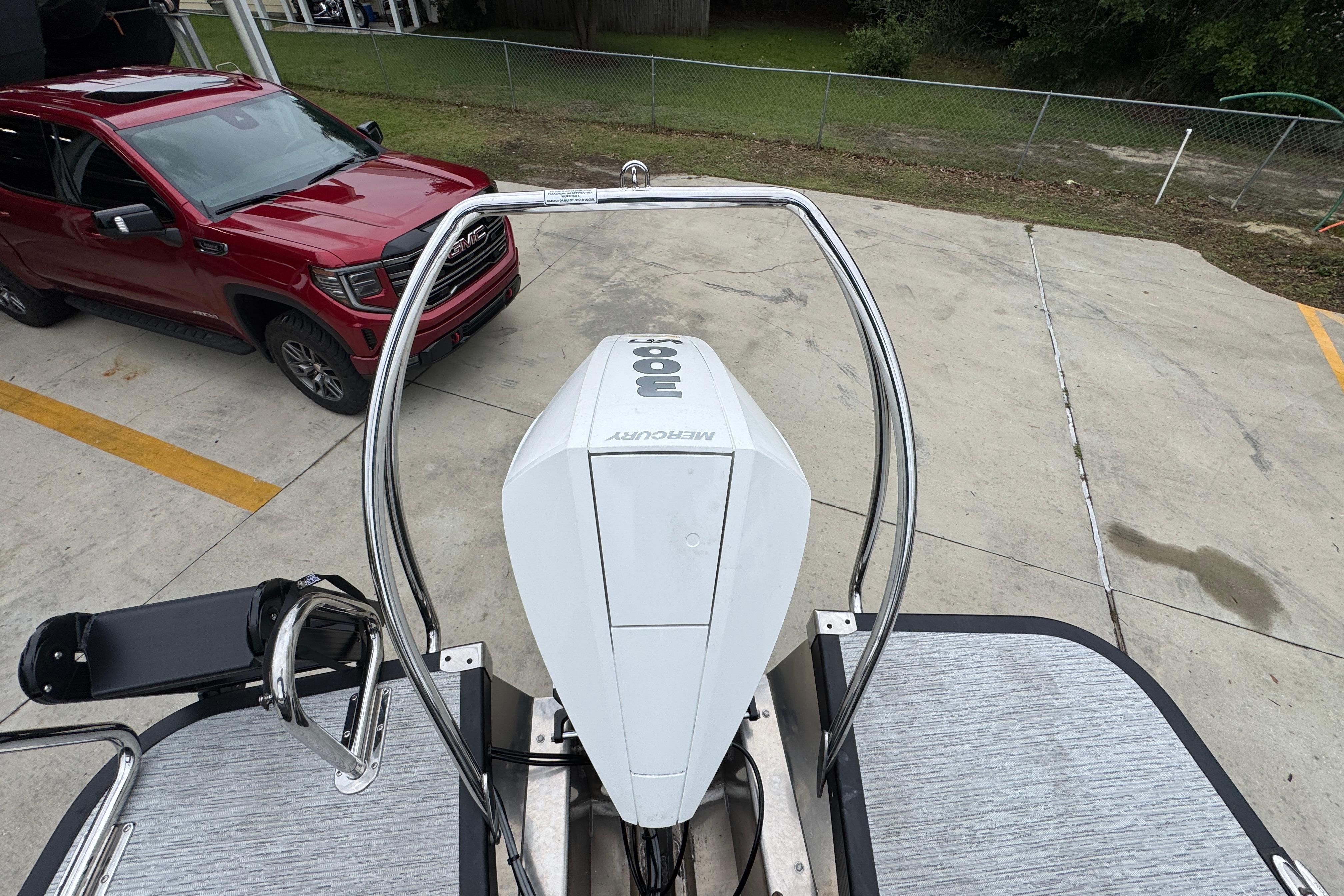 Top view of a 2027 Bennington 24 MFB boat with Mercury engine, parked beside a red vehicle.