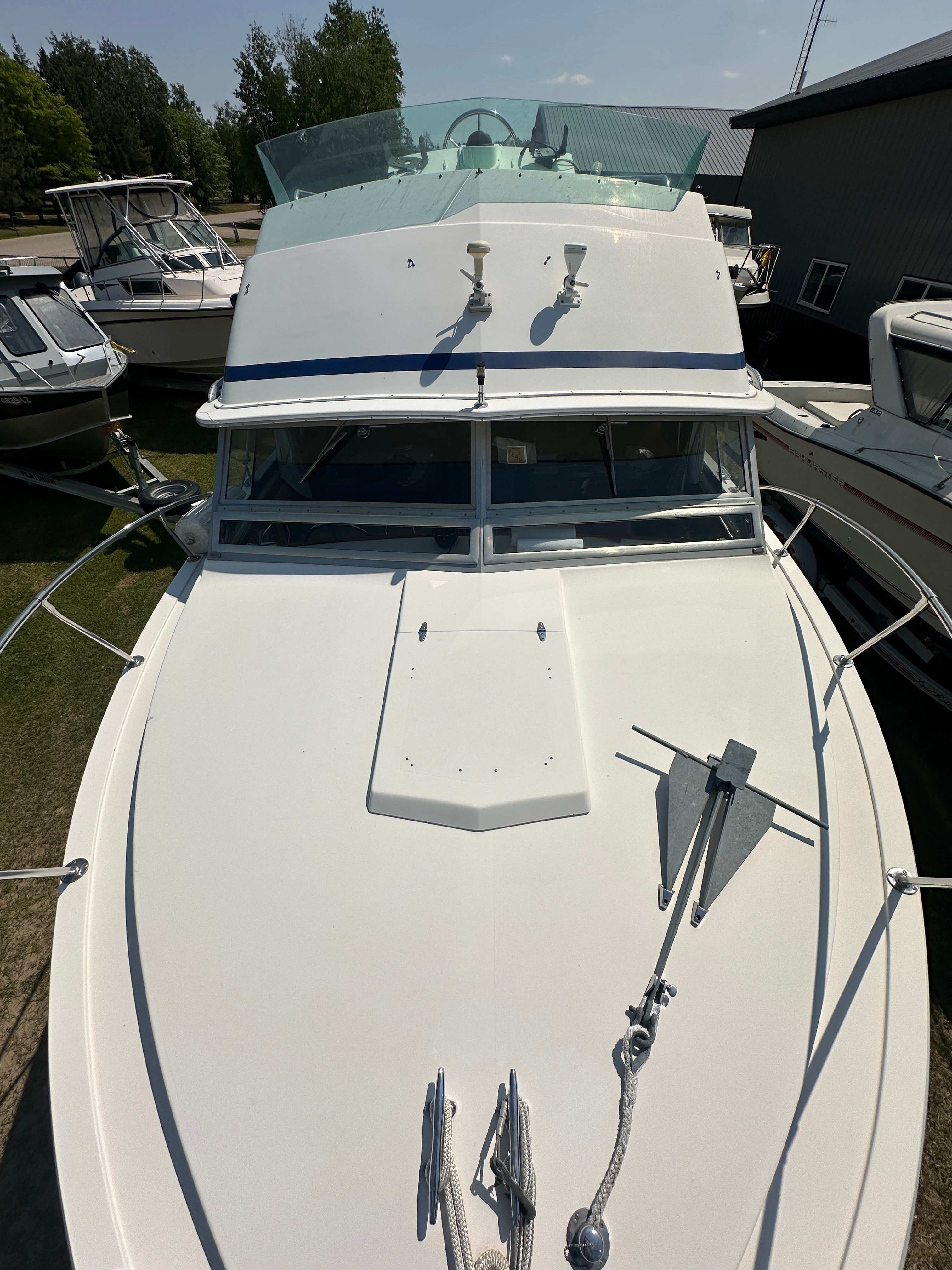 A 1983 Bertram Flybridge Cruiser with a white deck and anchor, surrounded by other boats.