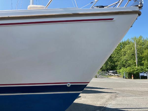 1989 Catalina 30 sailboat bow with red and blue stripes, parked on a sunny day.