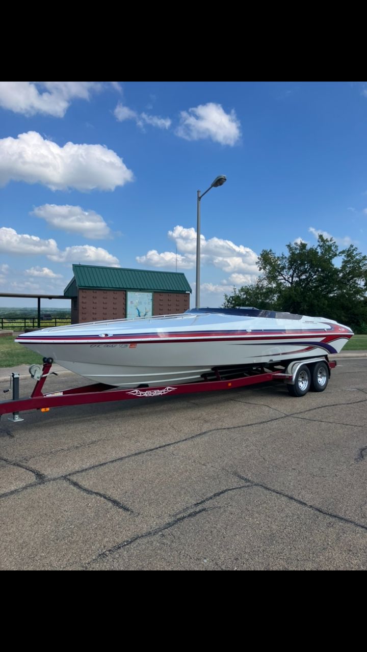 A white boat on a red trailer is parked on a lot under a blue sky.