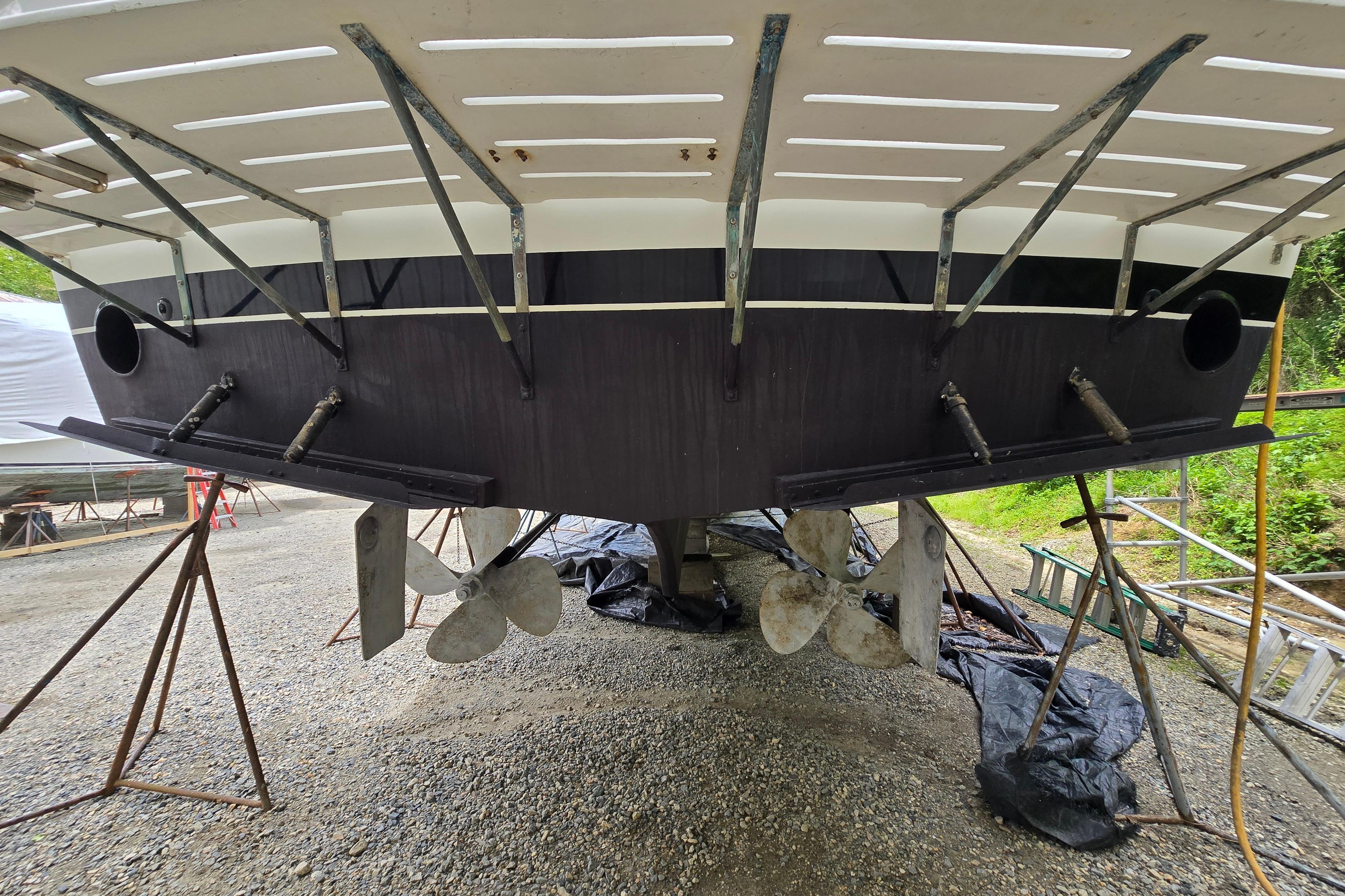 Stern view of a 1980 Hatteras 70 Motor Yacht on dry dock, showcasing propellers and rudders.