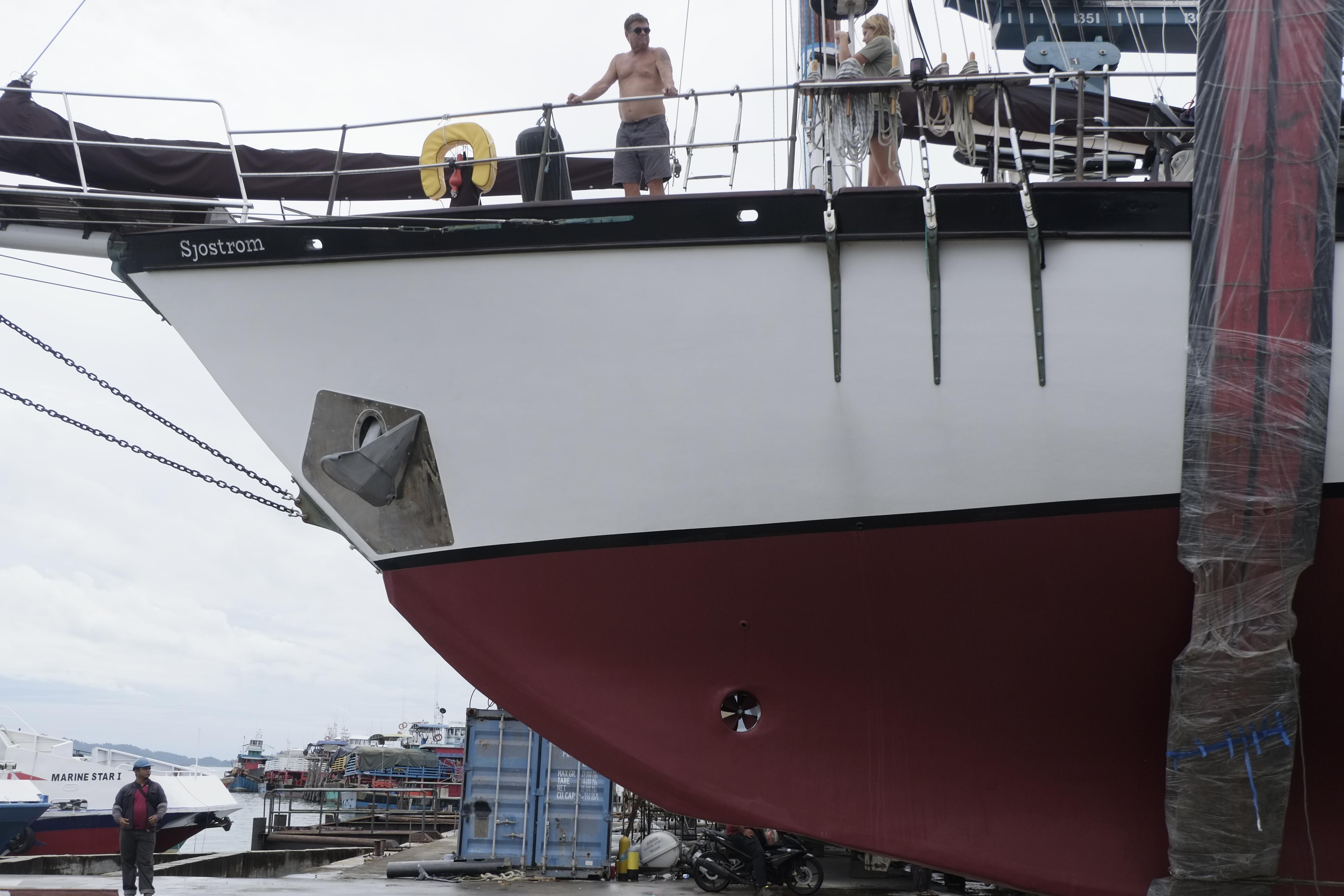 A 2006 Custom Bud Macintosh schooner docked, with people on deck, featuring a red hull.