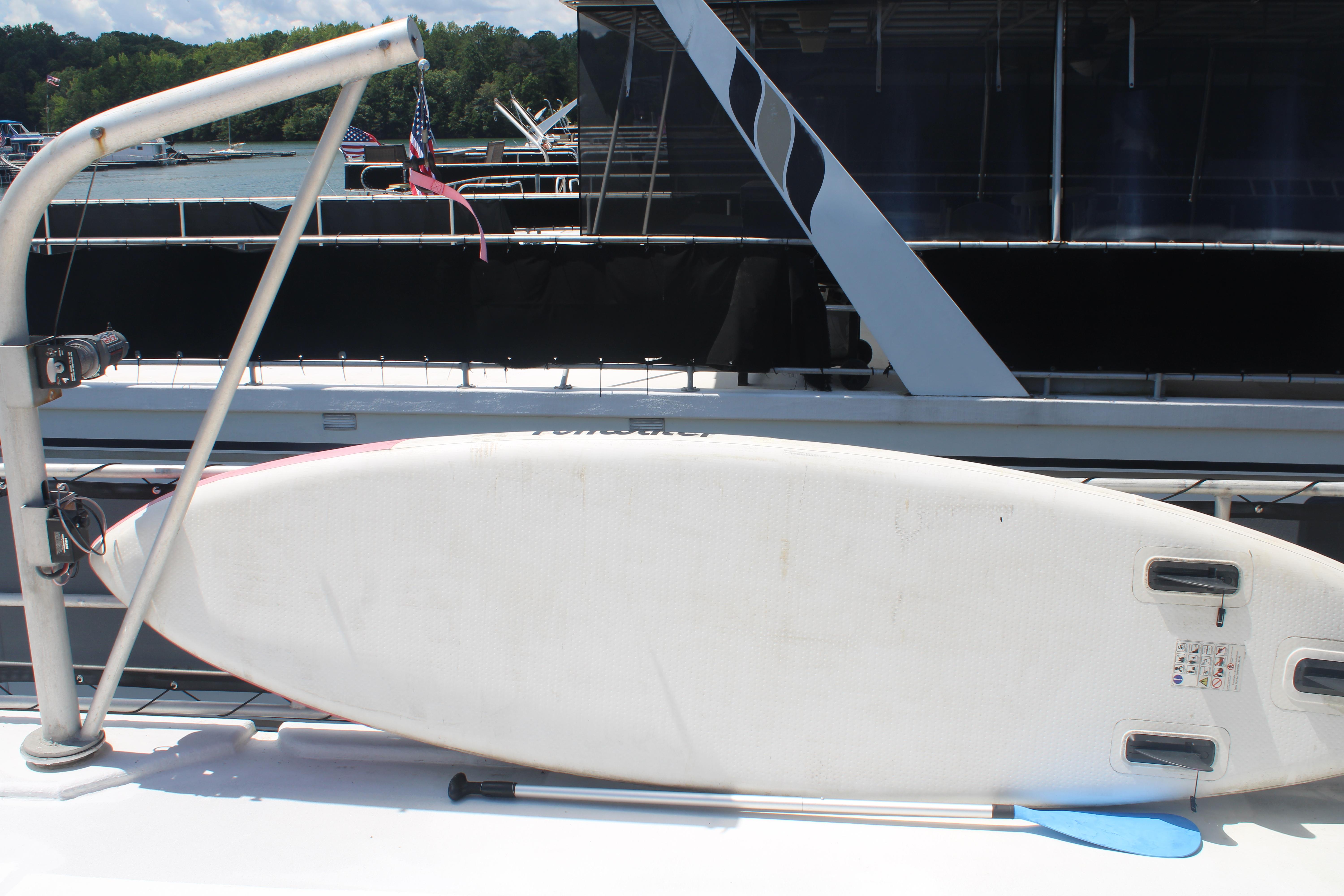 Surfboard on 1992 Sumerset 66 houseboat deck, docked by a lake.
