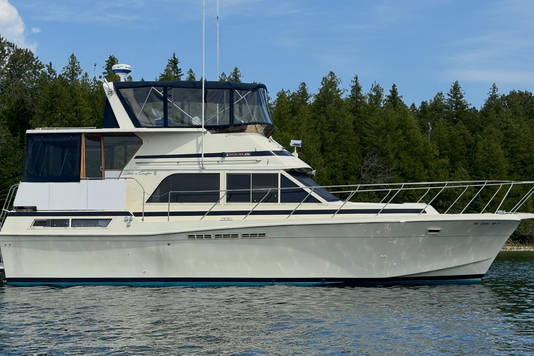 1987 Chris-Craft 427 Catalina yacht on calm water with forested background.