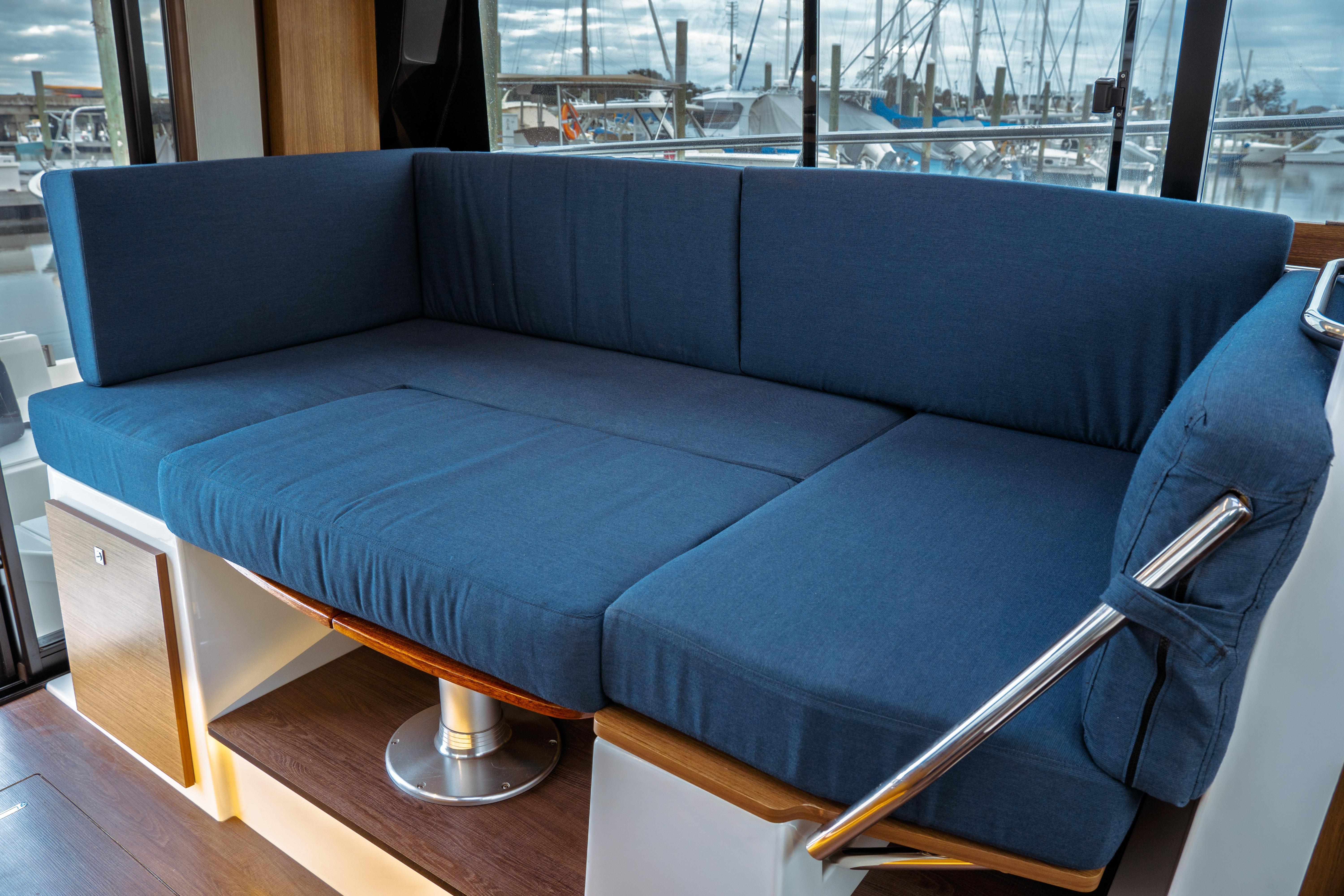 2019 Jeanneau NC 1095 interior with blue cushioned seating and marina view.