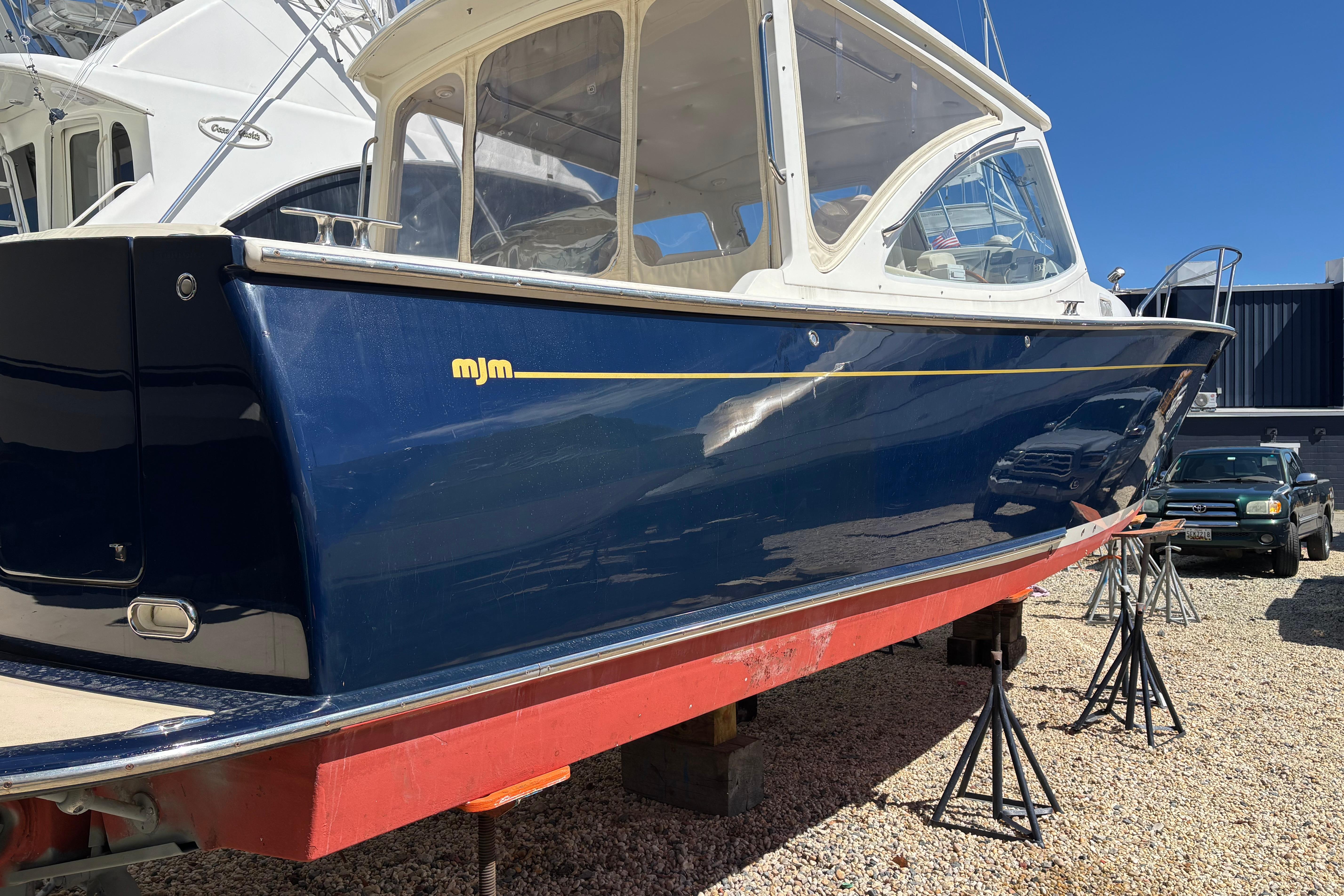 2006 MJM 34z Express HT boat on stands, blue hull, sunny day.
