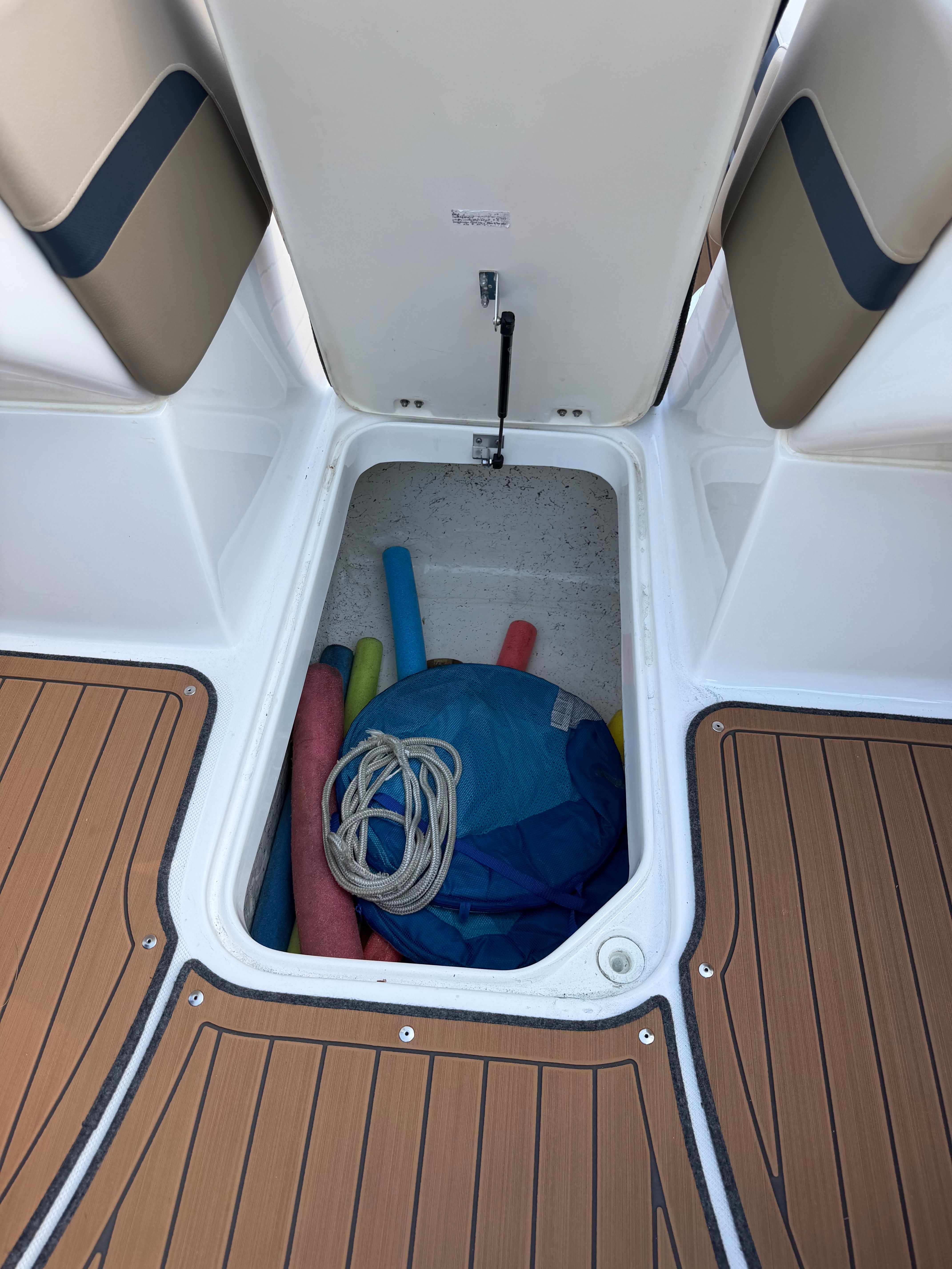 An open storage compartment on a boat with pool noodles and a rope.