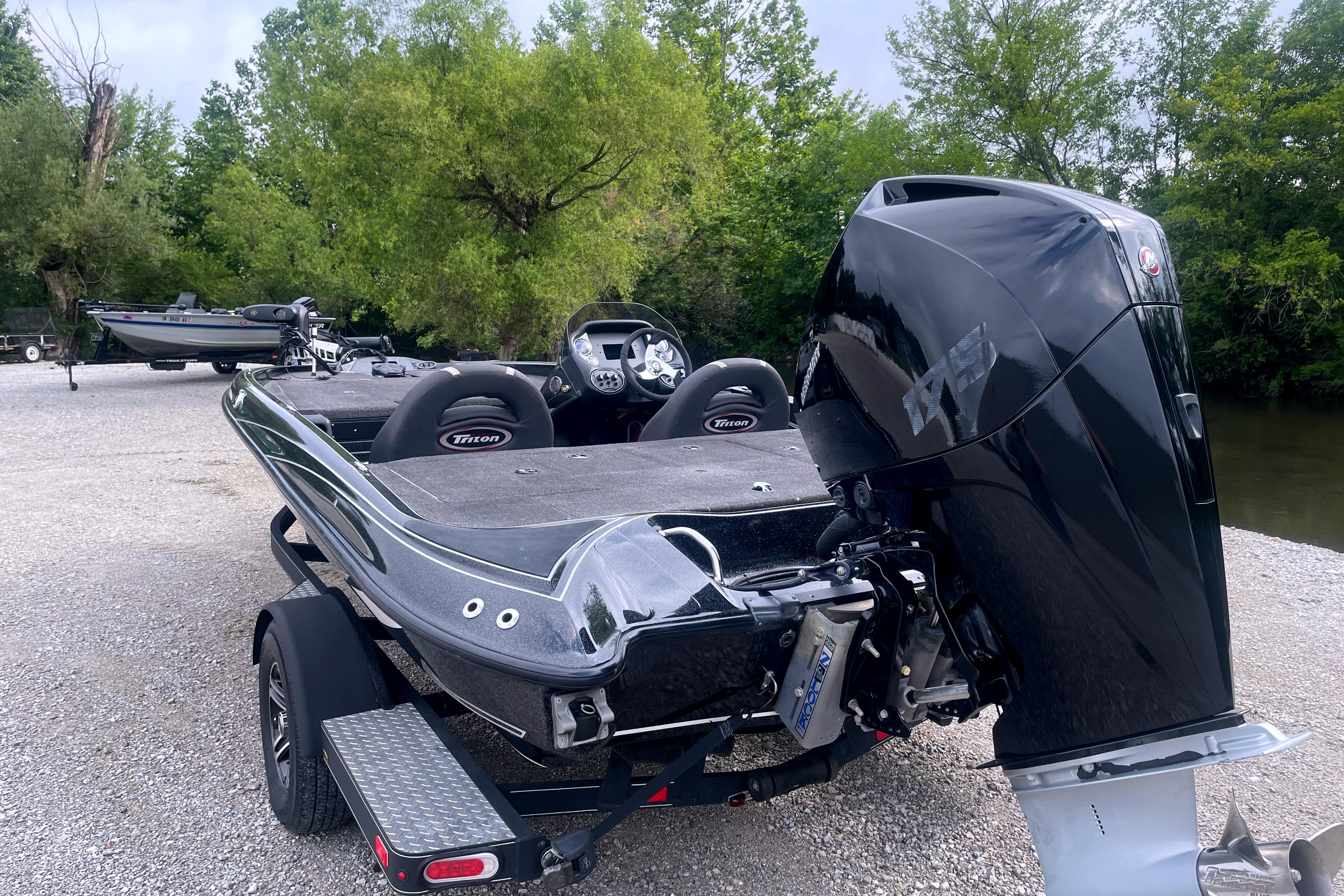 2022 Triton 18 TrX boat with powerful outboard motor, parked on gravel near trees.
