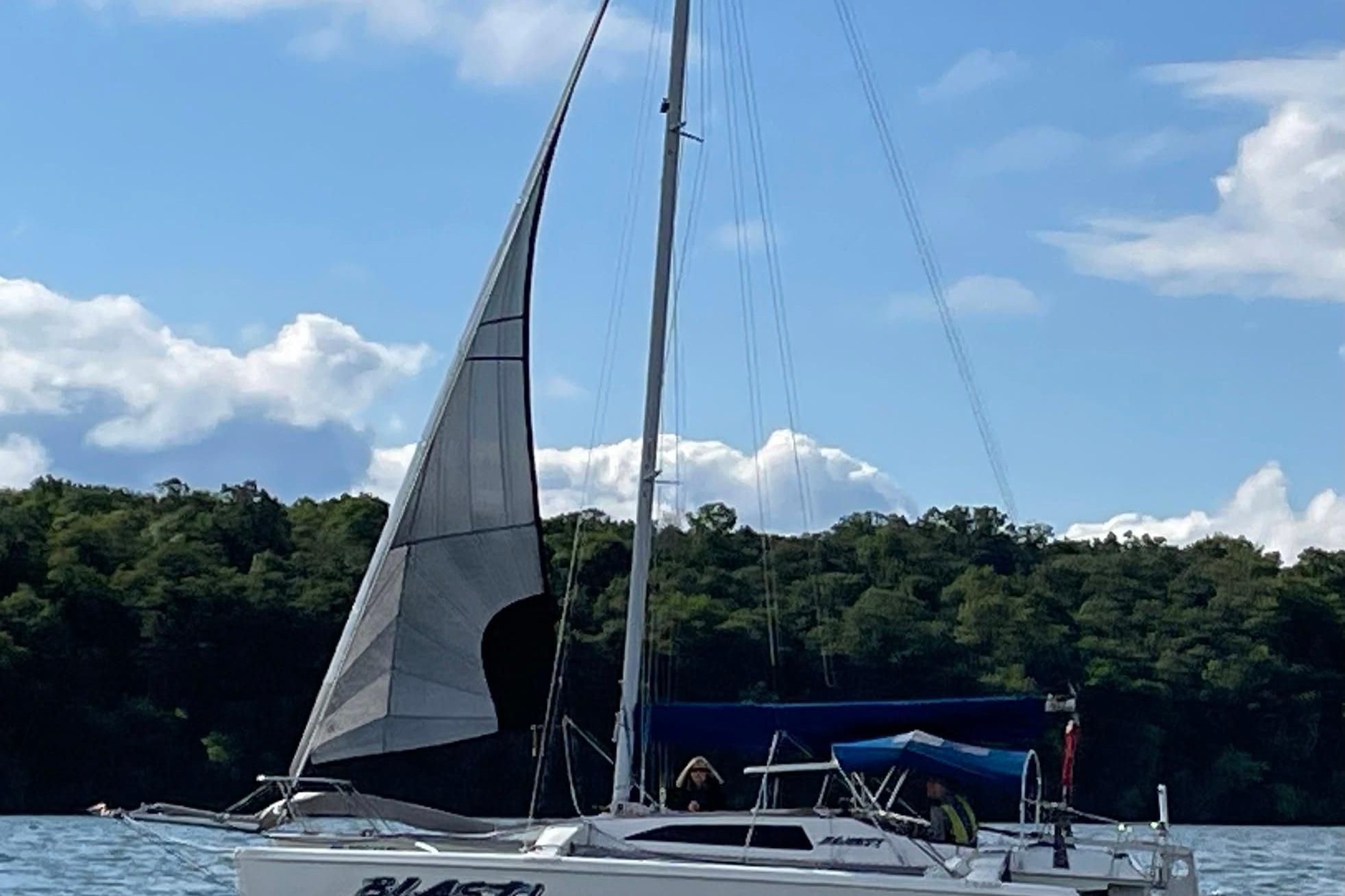 Sailboat Corsair F-27, 1993 model, sailing on a lake with forested shoreline.