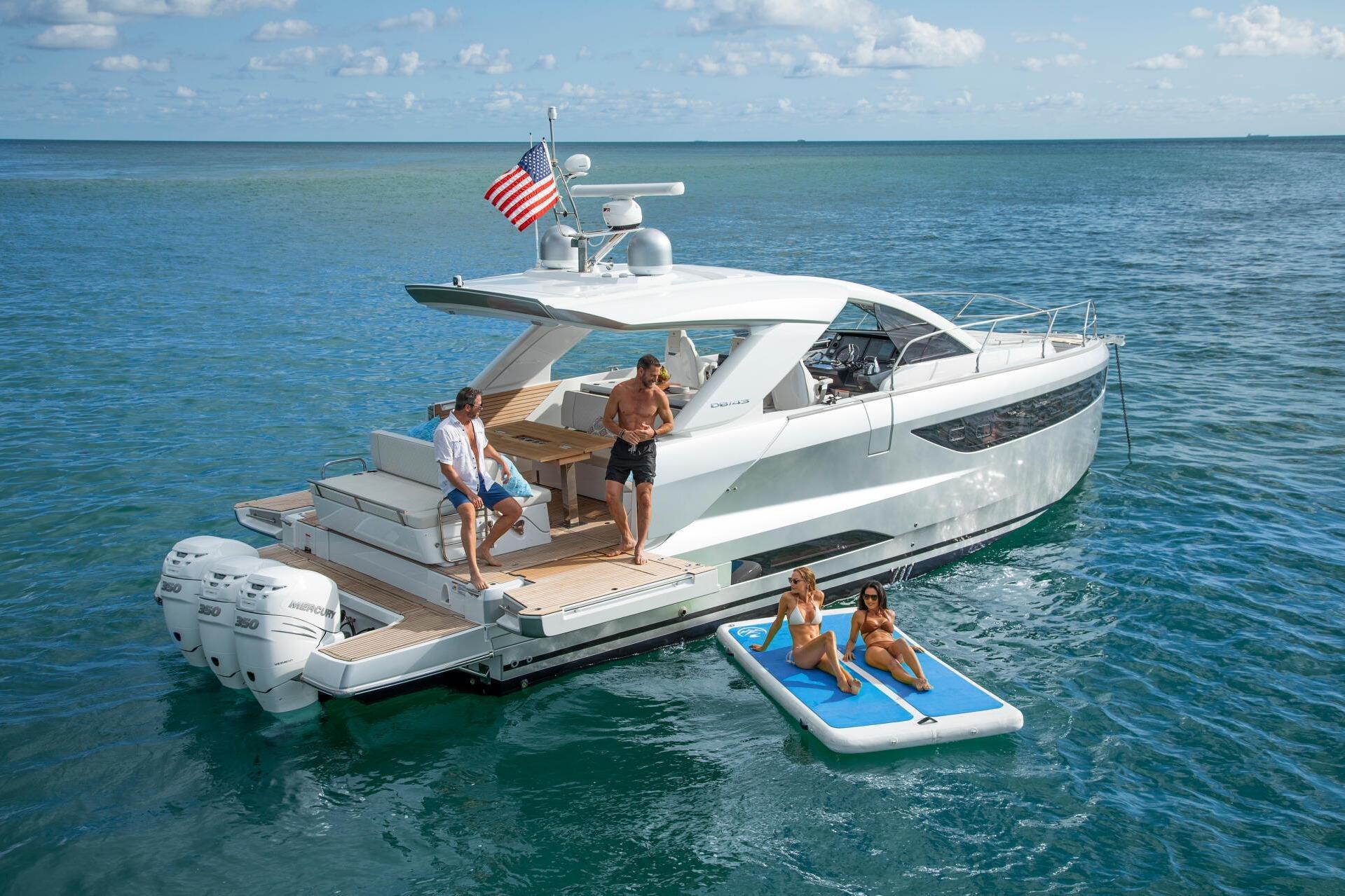 2027 Jeanneau DB/43 OB yacht with people relaxing on deck and floating mat.