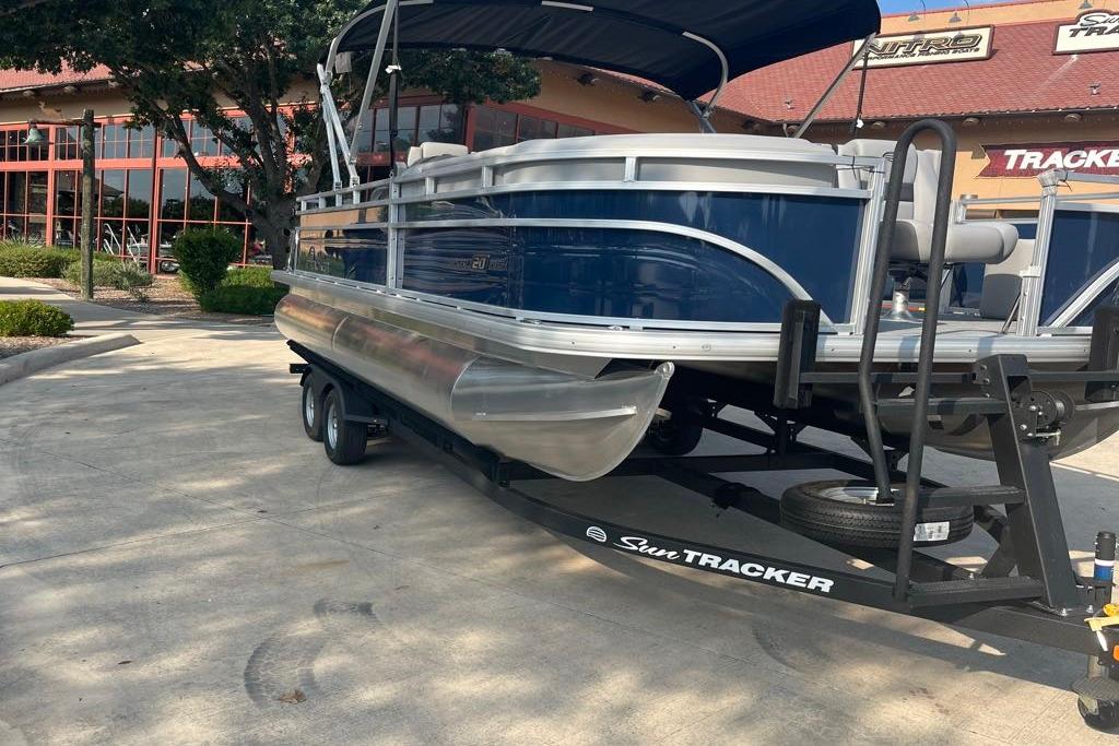 2026 Sun Tracker SportFish 20 DLX pontoon boat on trailer, parked outside dealership.