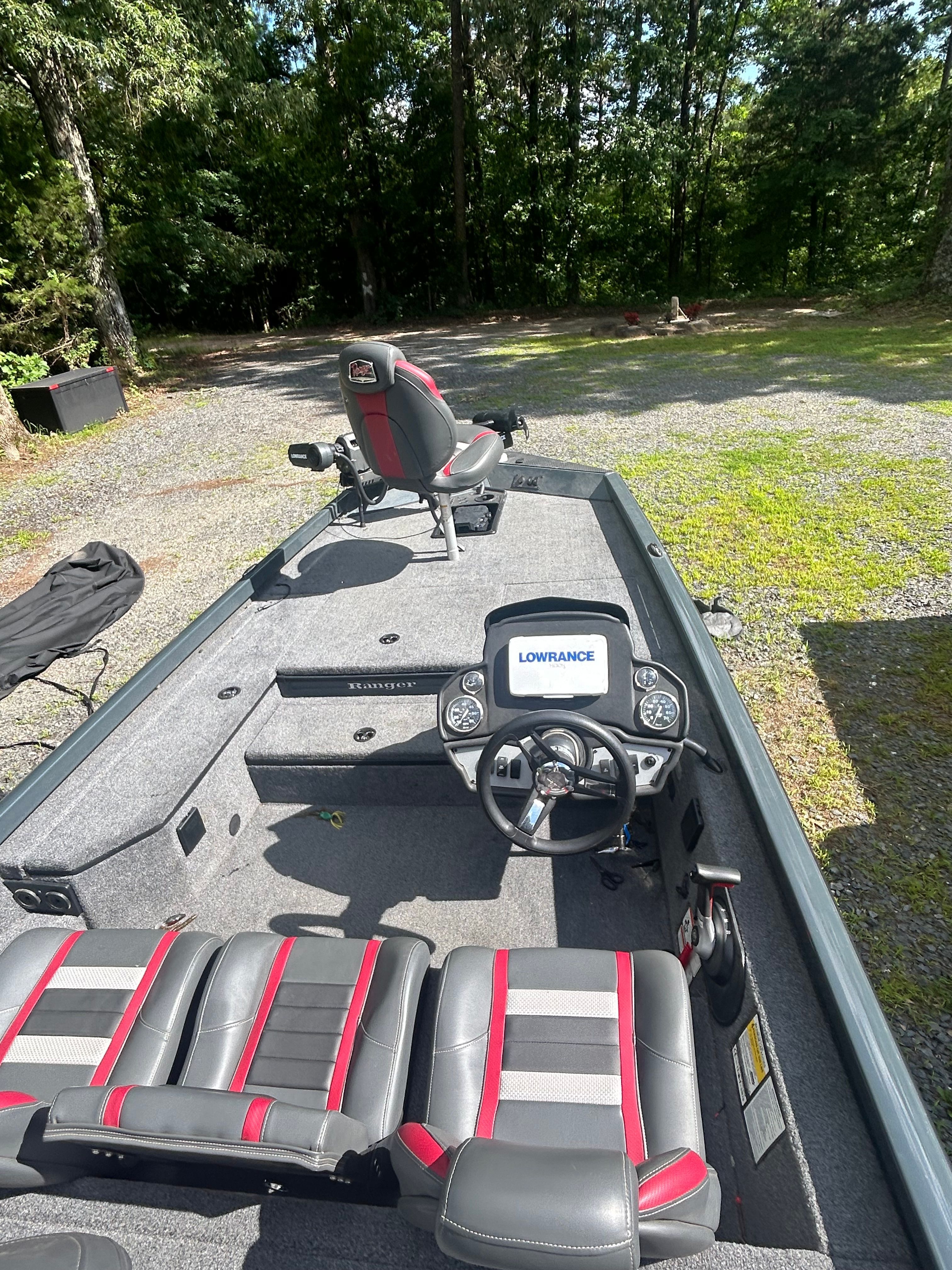 A Ranger RT178 boat with gray and red seats, parked on a wooded property.