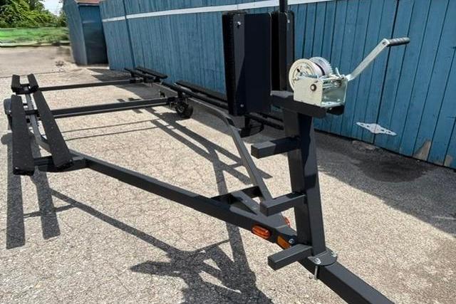 2023 Yacht Club 18' Pontoon trailer, black frame, parked on pavement near blue fence.