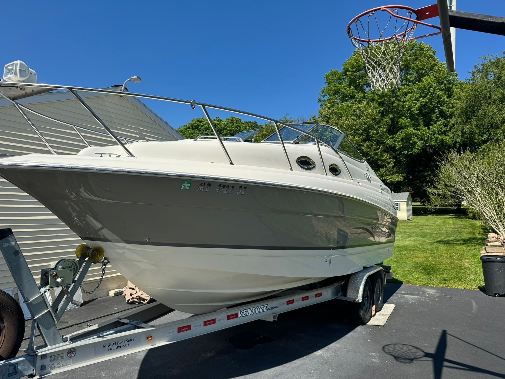A white boat on a trailer next to a basketball hoop.