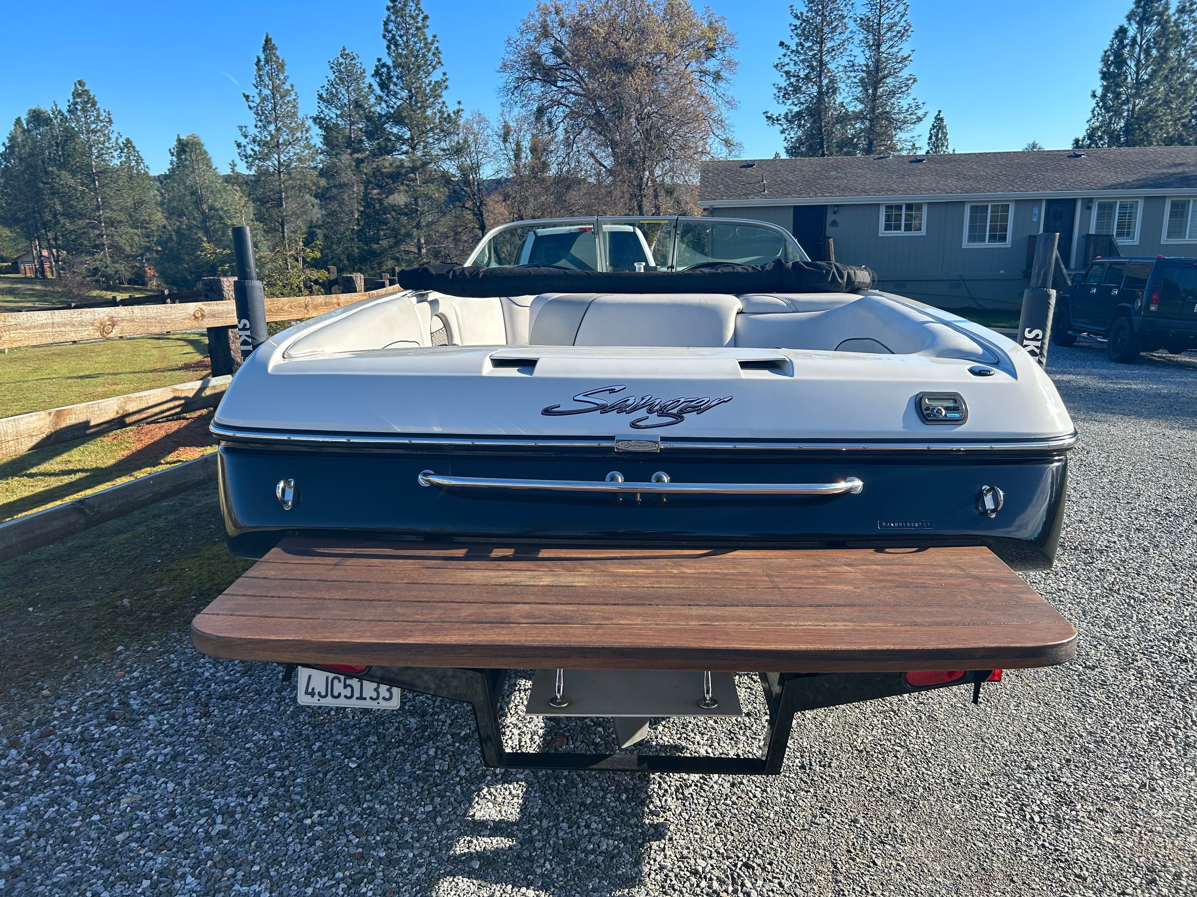 A 2007 Sanger boat is parked on a gravel lot in front of a house.