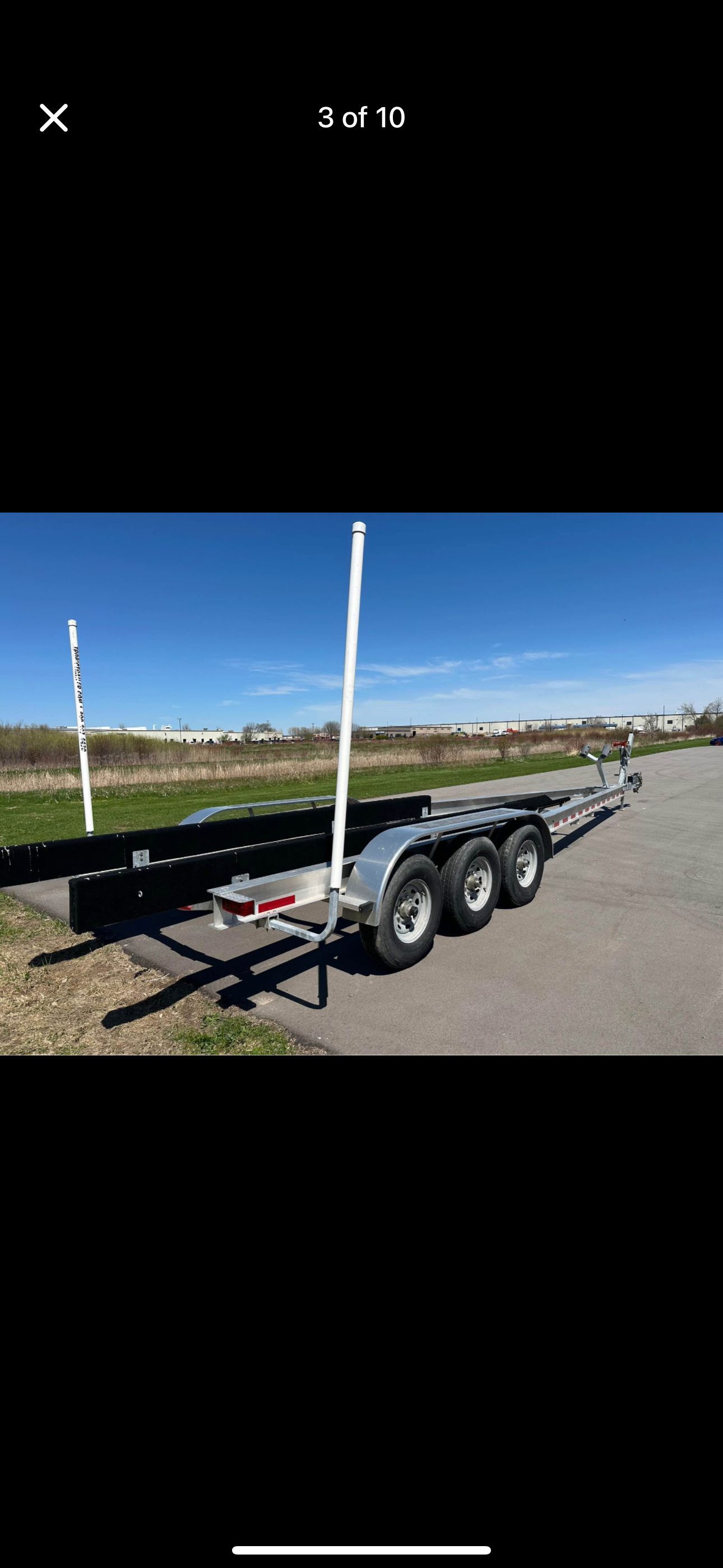 A triple-axle boat trailer is parked on a paved area under a clear sky.